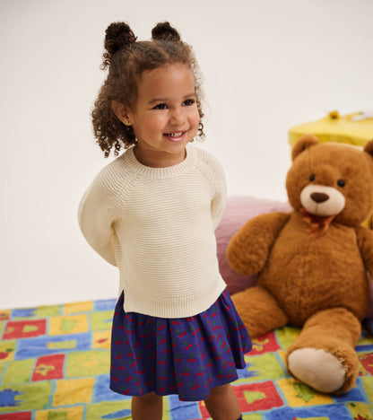 Toddler girl wearing a cream knit sweater dress with a purple cherry-print skirt