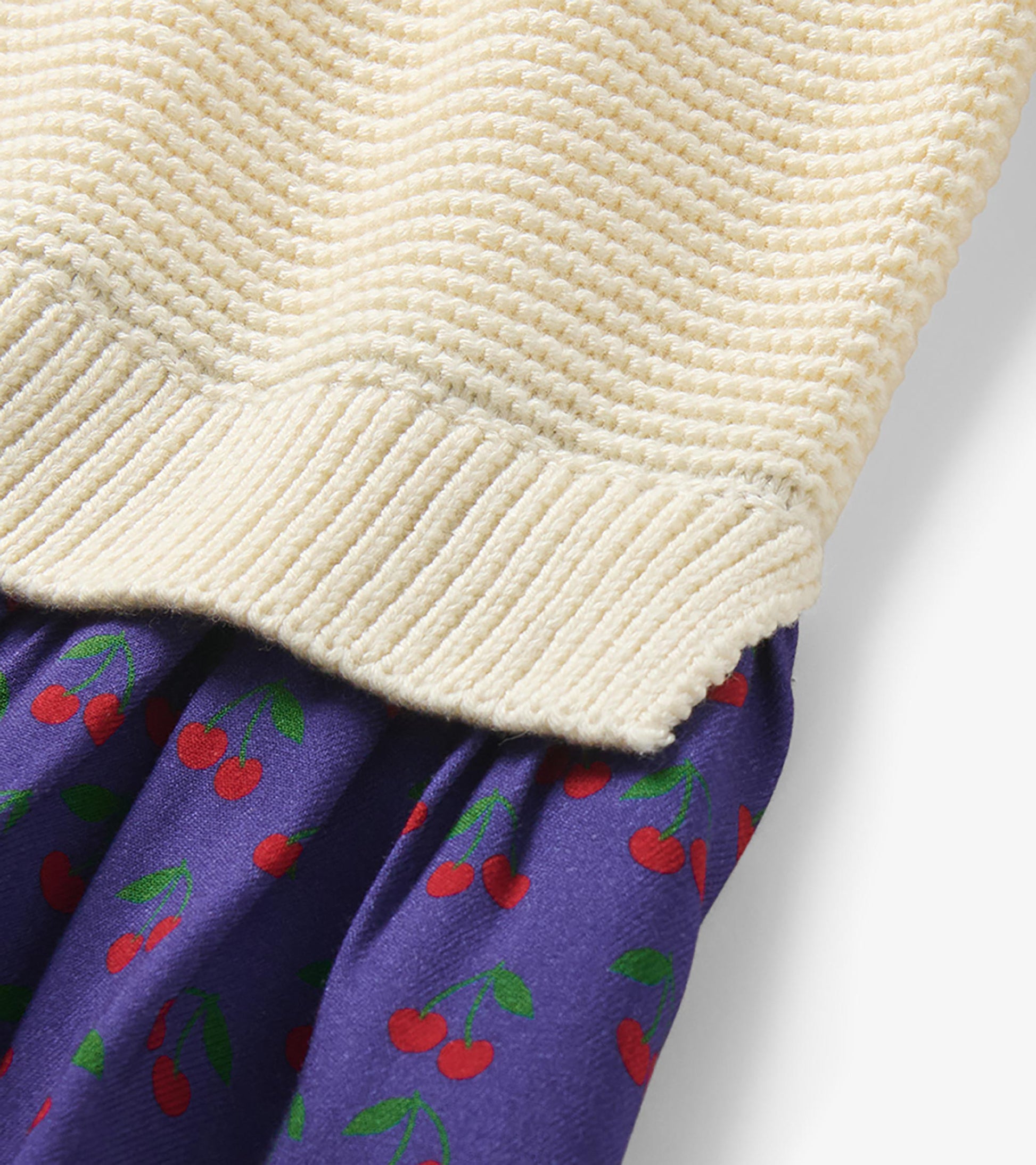Close-up of the cream knit hem and purple skirt with red cherry print