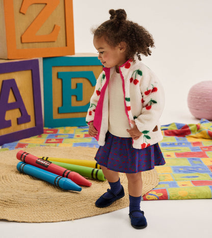Toddler wearing a cream sherpa jacket with red cherry print and pink zipper trim