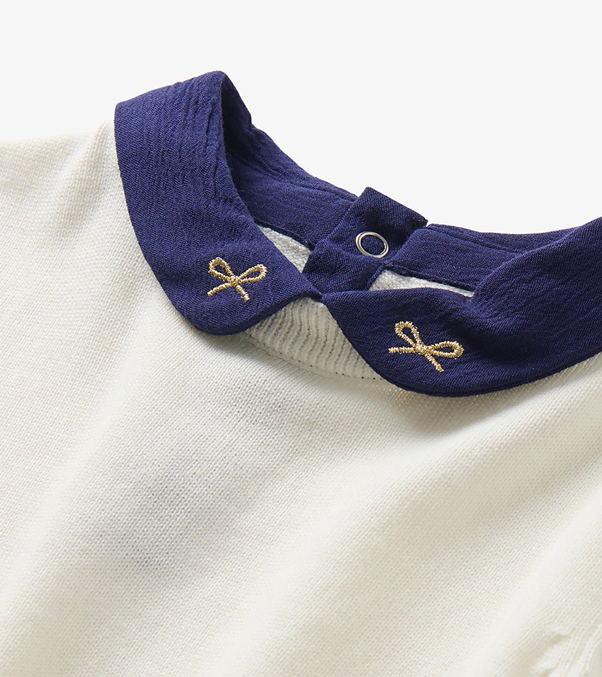 Close-up of navy Peter Pan collar with gold bow embroidery and back snap detail on cream sweater