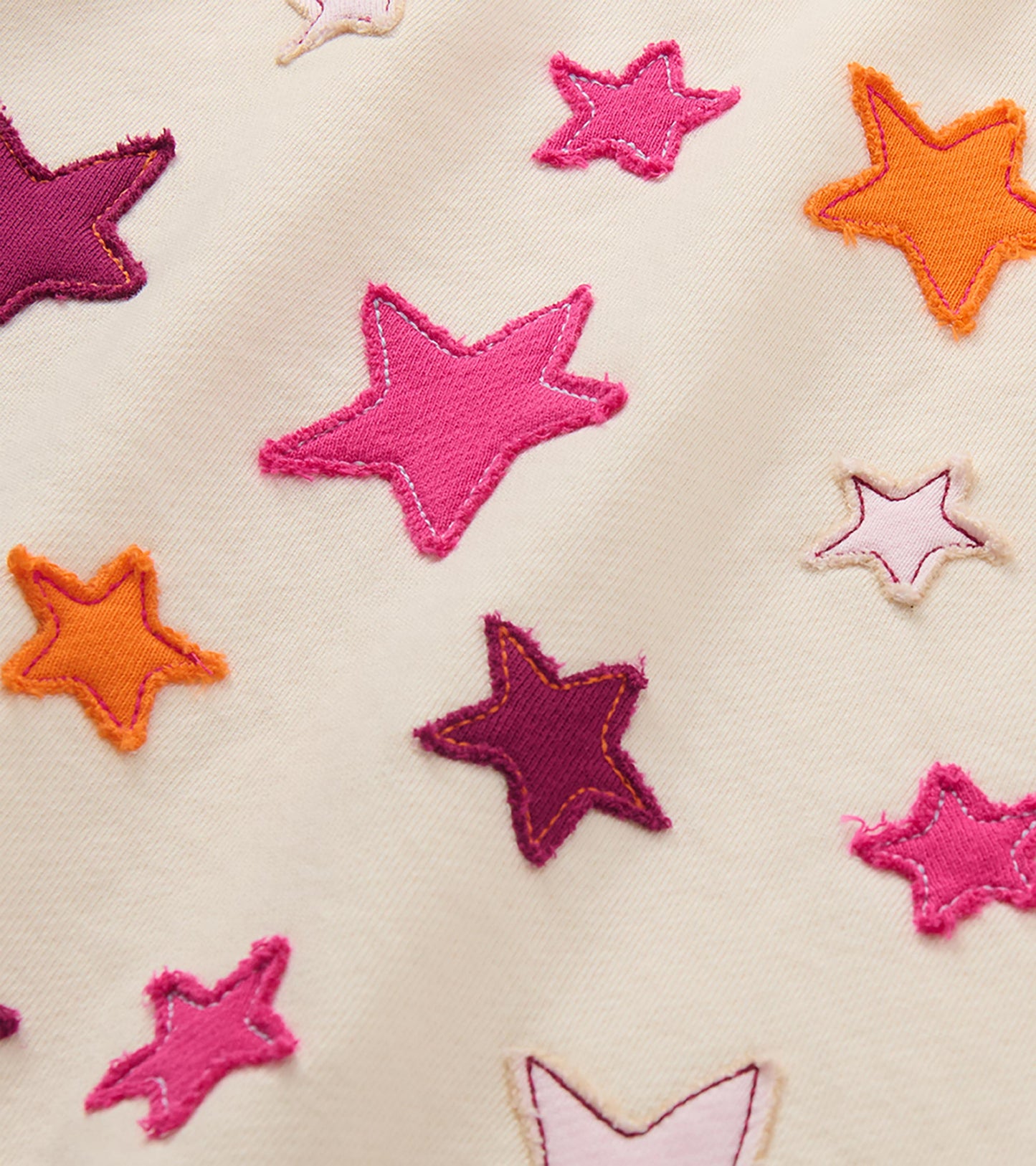 Close-up of pink, plum, orange, and pale pink star appliques on a cream pullover