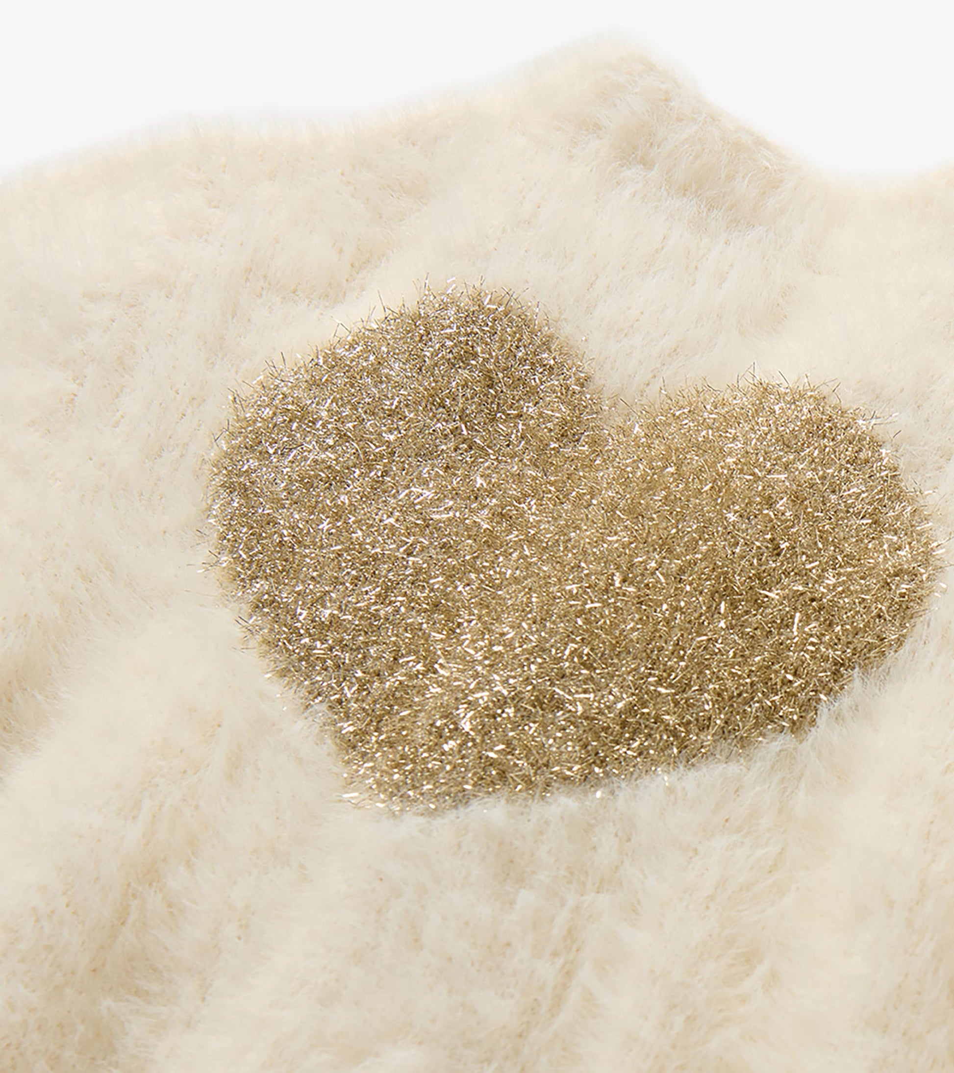 Close-up of glittery gold heart detail on cream fuzzy knit cardigan