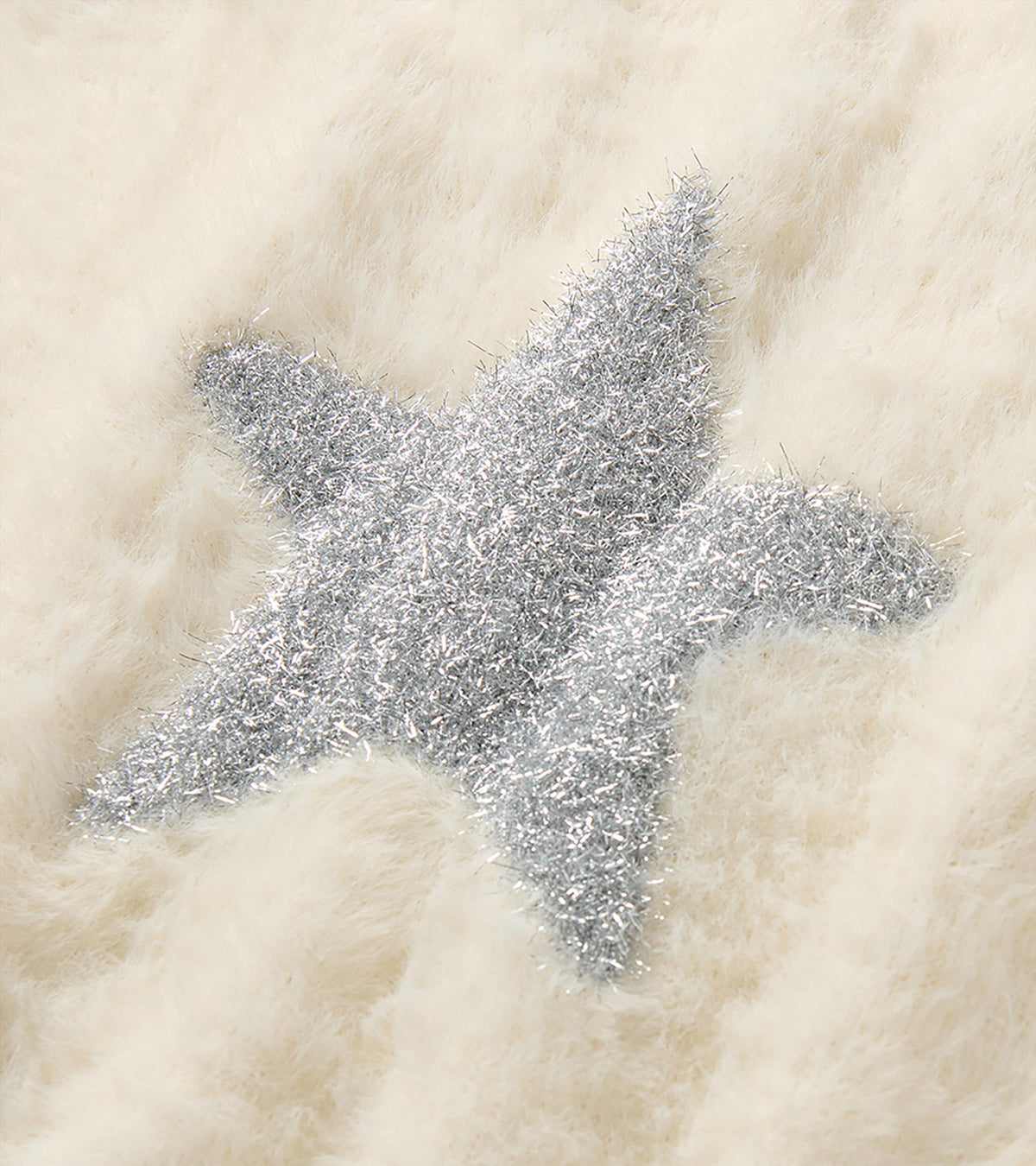 Close-up of the silver star detail on the cream sweater vest