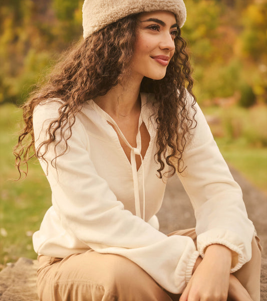 Cream long sleeve top with tie neckline, shown worn outdoors in a close-up side view