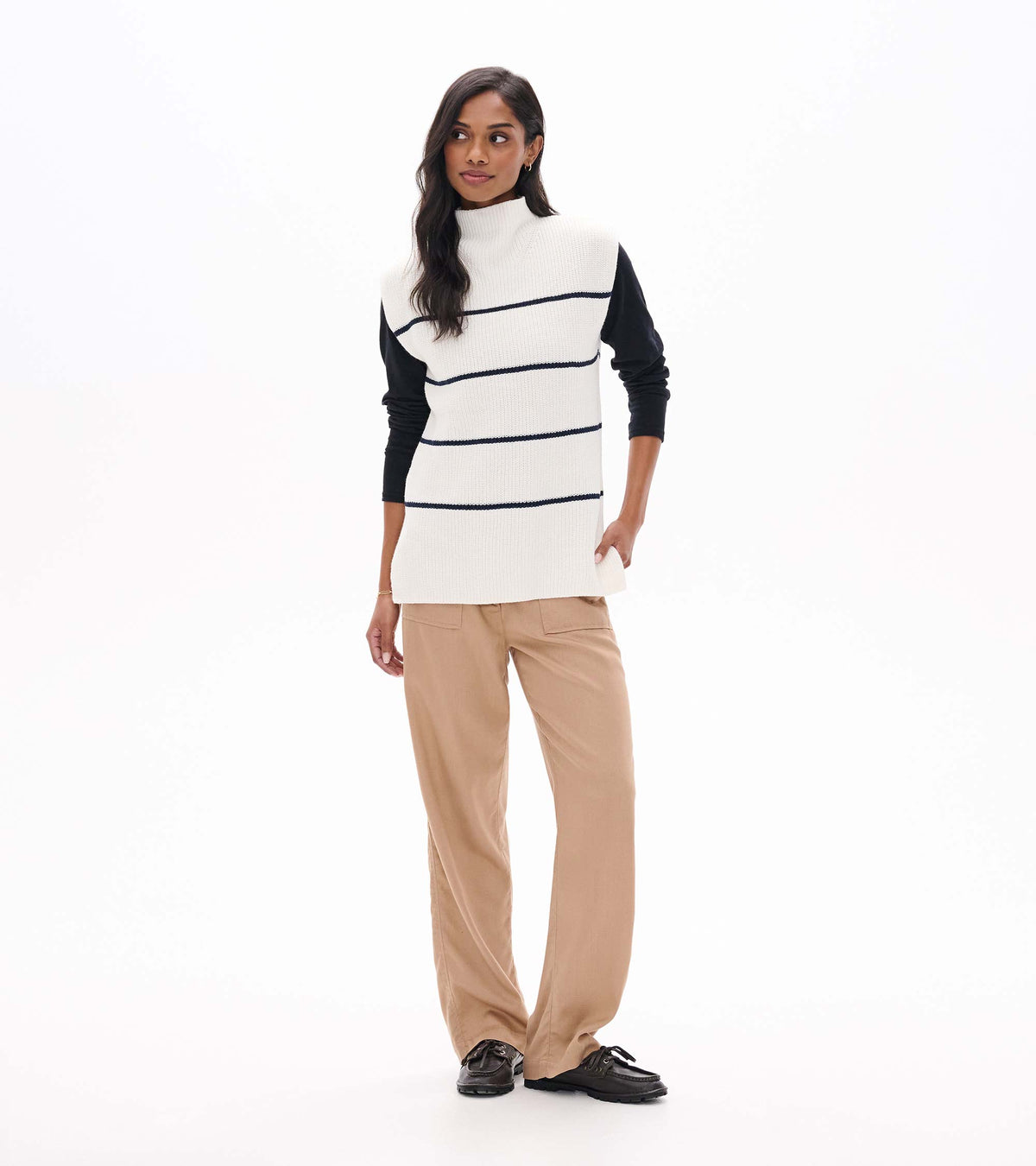 Front view of cream sleeveless striped sweater tunic layered over a black long sleeve top