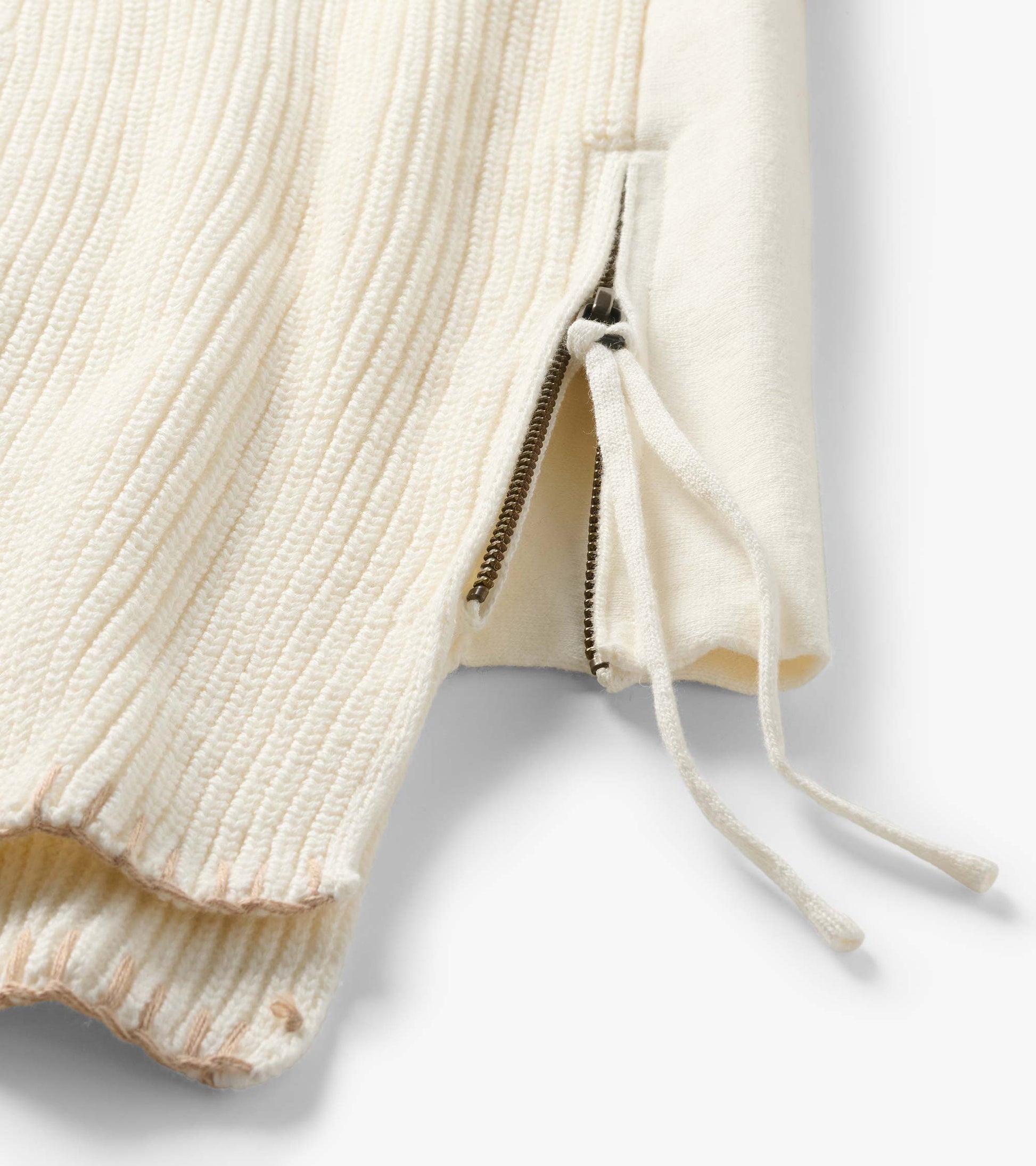 Close-up of cream sweater side hem with zip opening and tie detail
