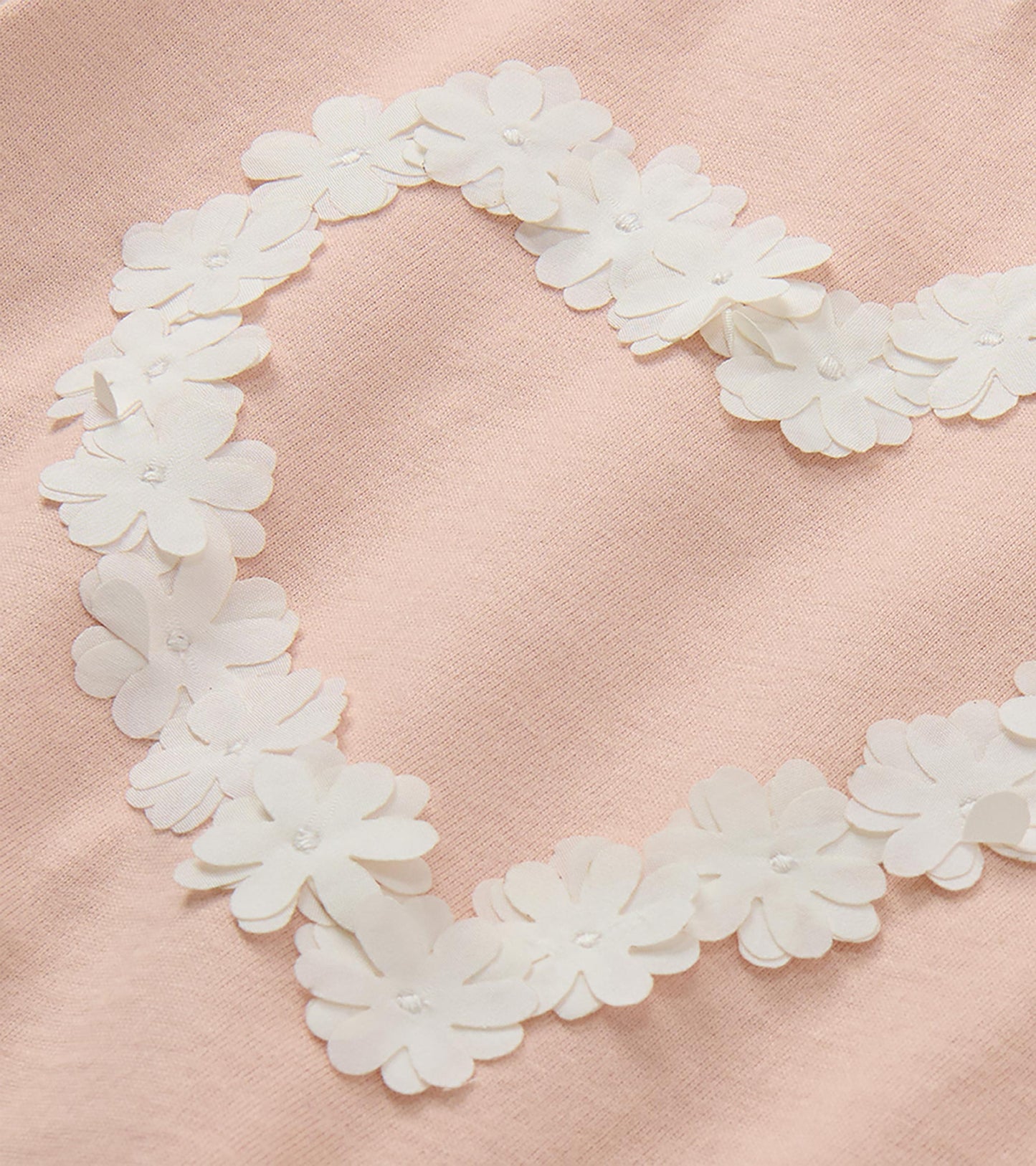 Close-up of white floral applique heart detail on blush pink T-shirt