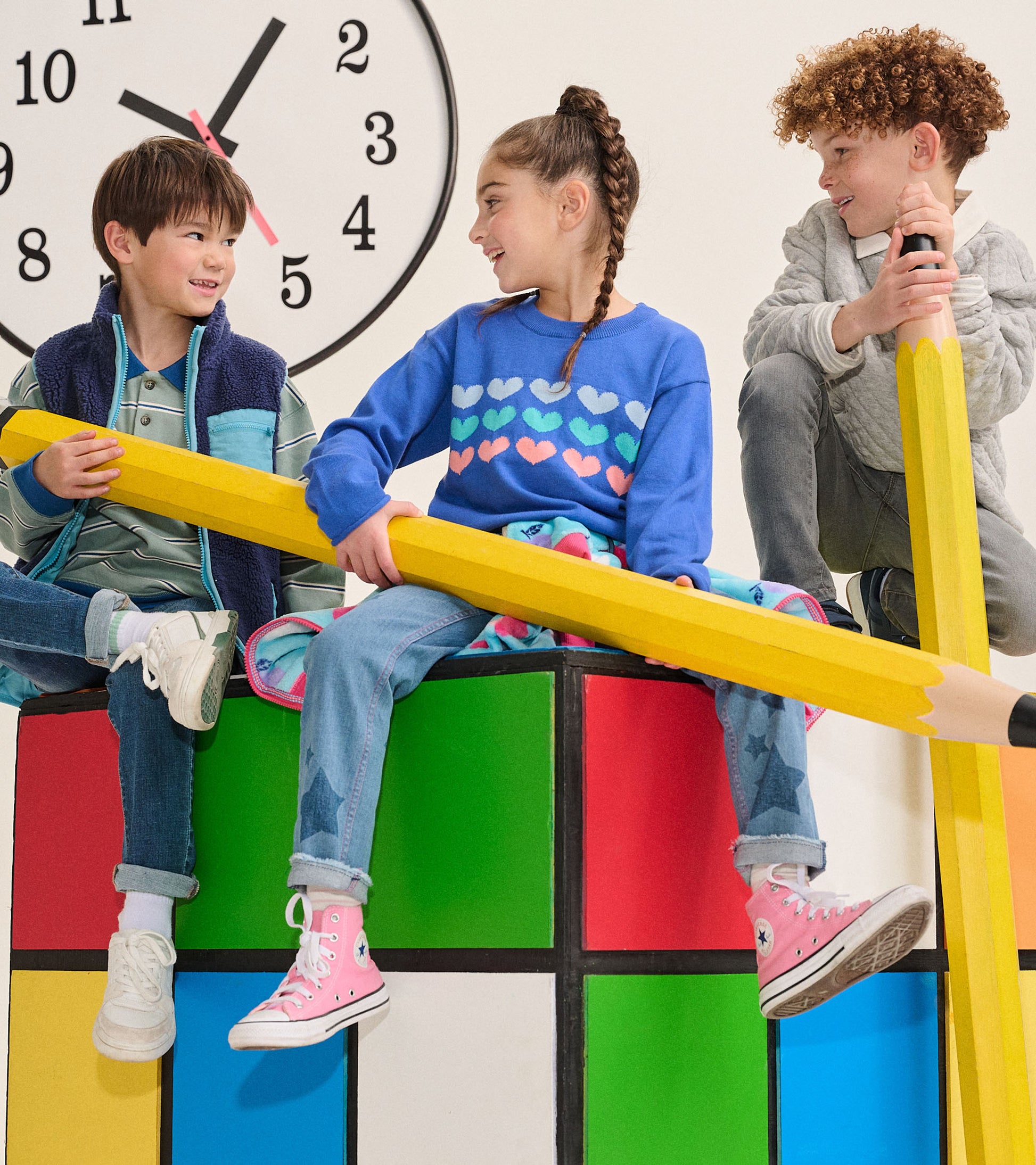 Girl wearing royal blue heart stripe crew neck sweater seated with other kids on colorful blocks