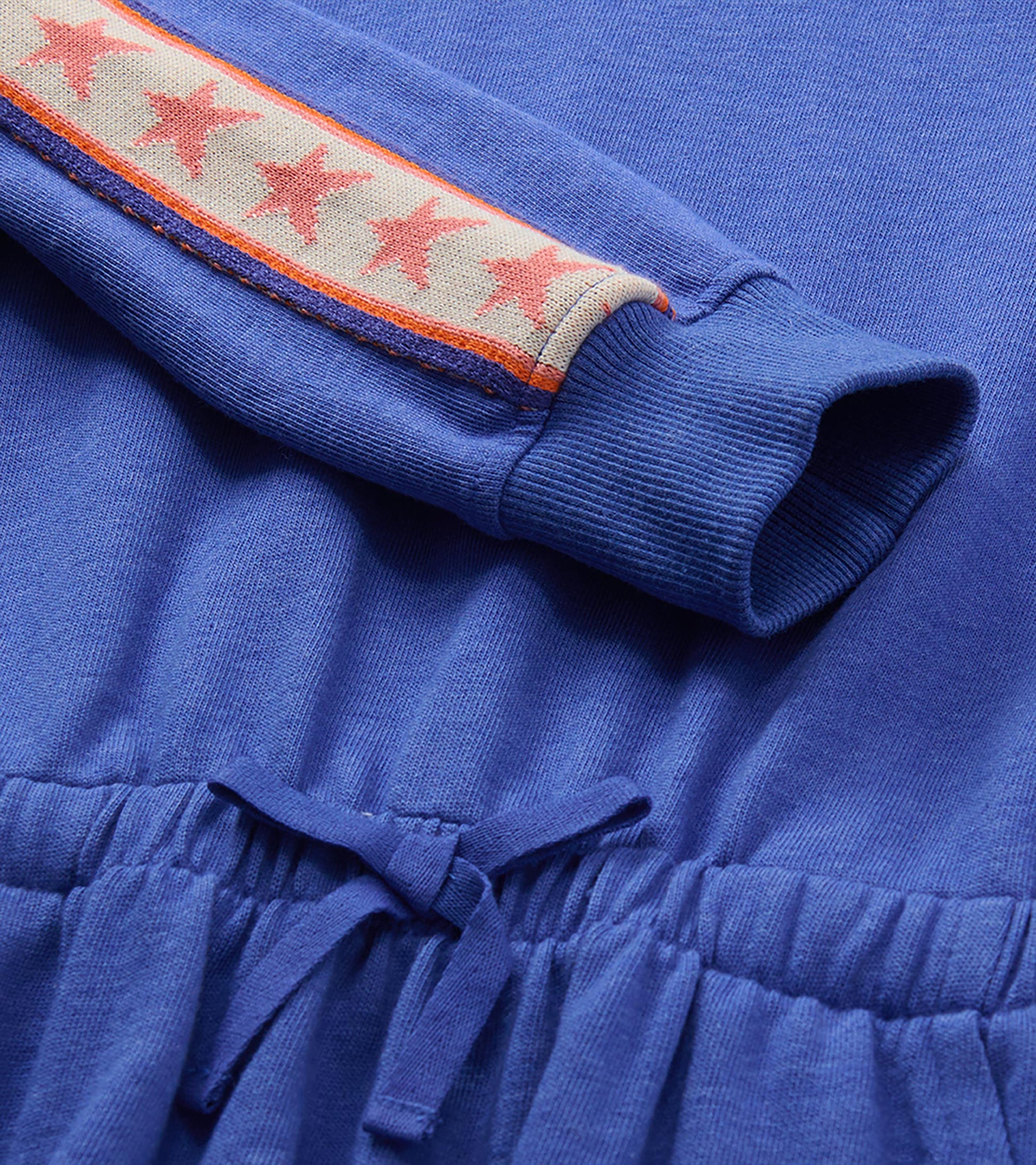 Close-up of blue dress sleeve with pink star trim, ribbed cuff, and elastic waist tie detail