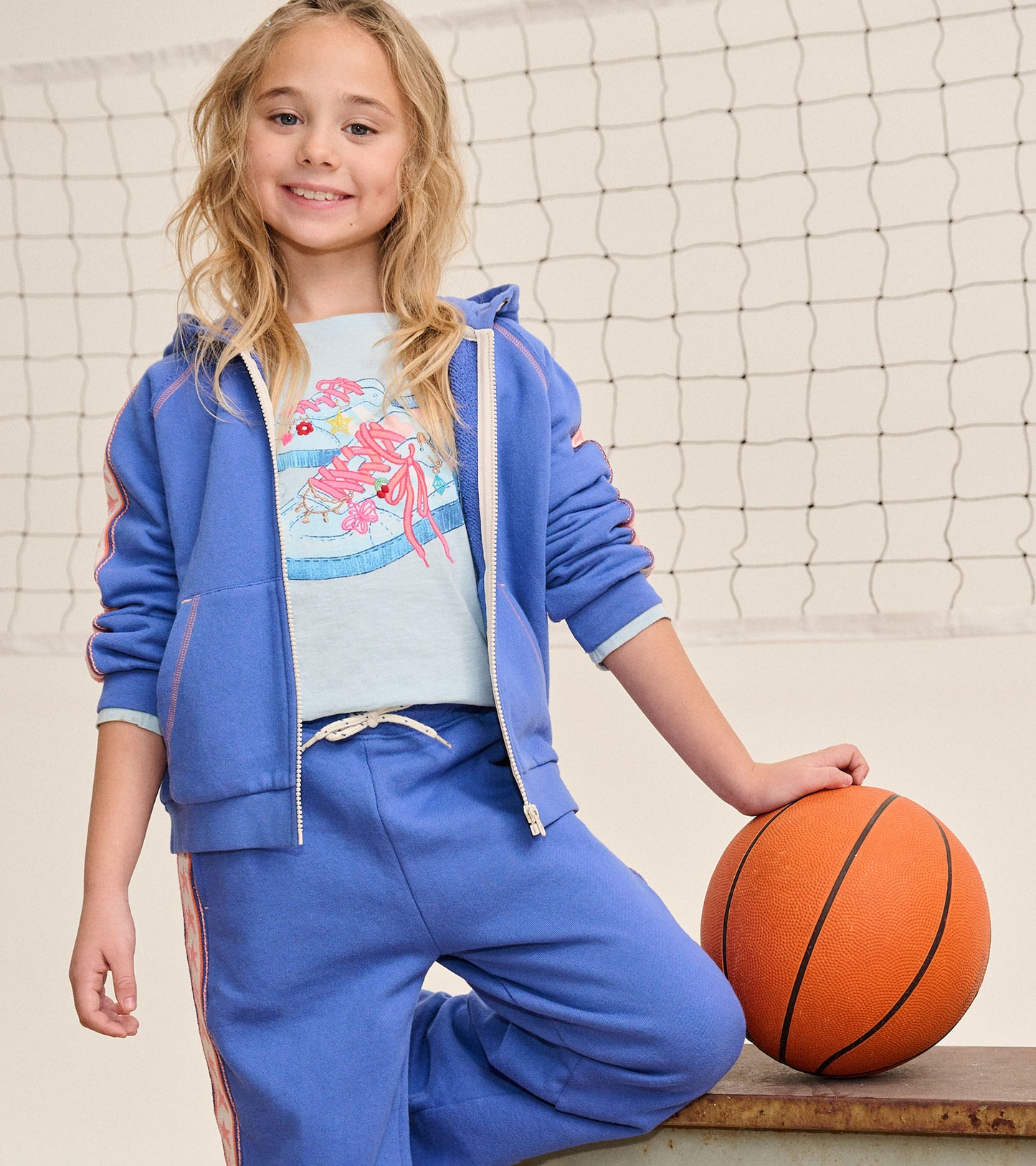 Girl wearing blue wide leg track pants with pink star side stripes beside a basketball