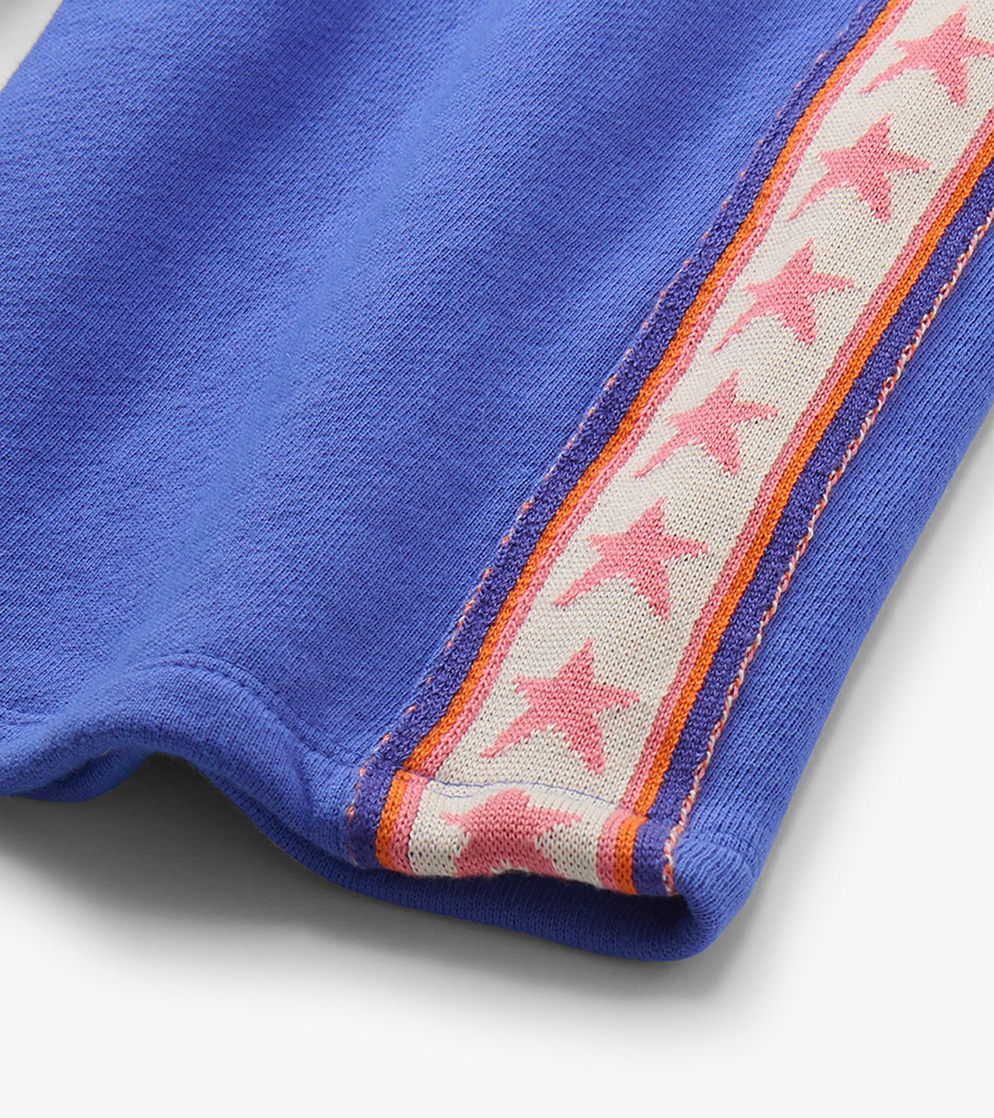 Close-up of blue track pants with pink star side stripe and orange trim