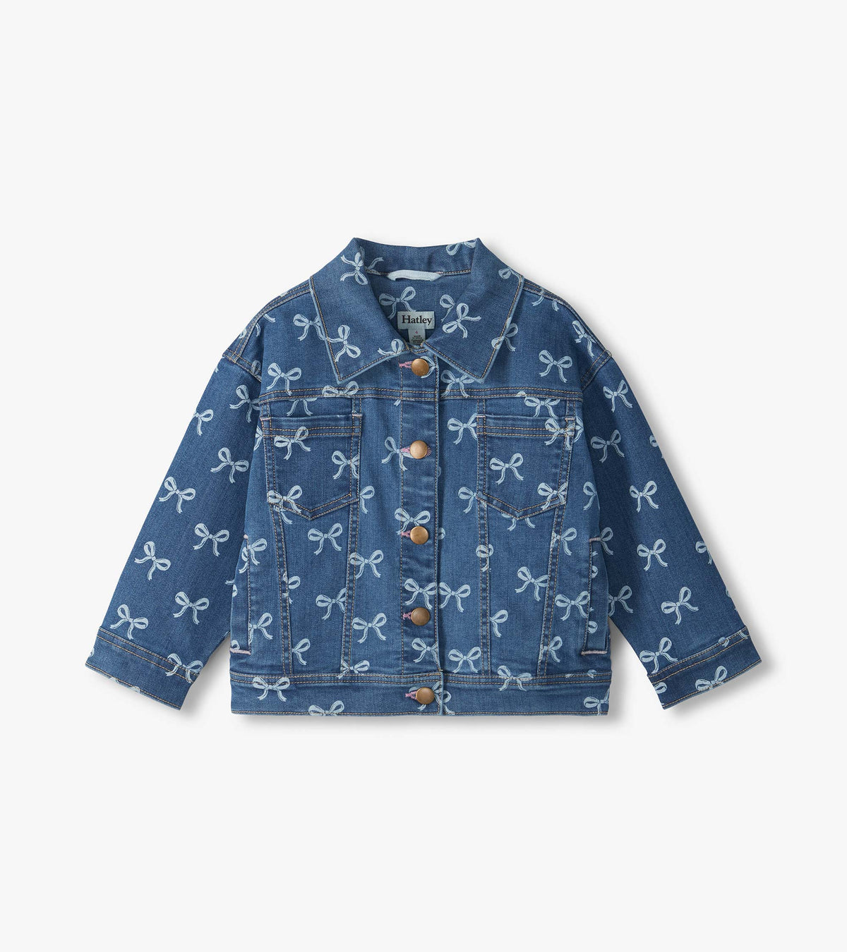 Front view of blue slouchy denim jacket with white bow print, chest pockets and brass-tone buttons