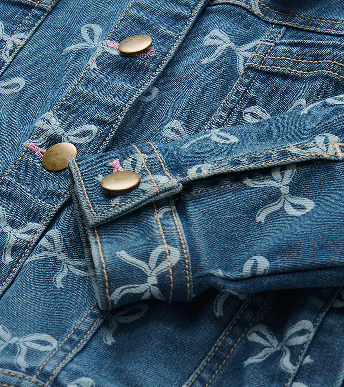 Close-up of blue bow-print denim jacket with brass-tone buttons and contrast stitching
