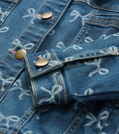 Close-up of blue bow-print denim jacket with brass-tone buttons and contrast stitching