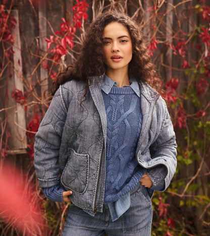 Close view of stellar blue cable knit sweater under a gray quilted jacket