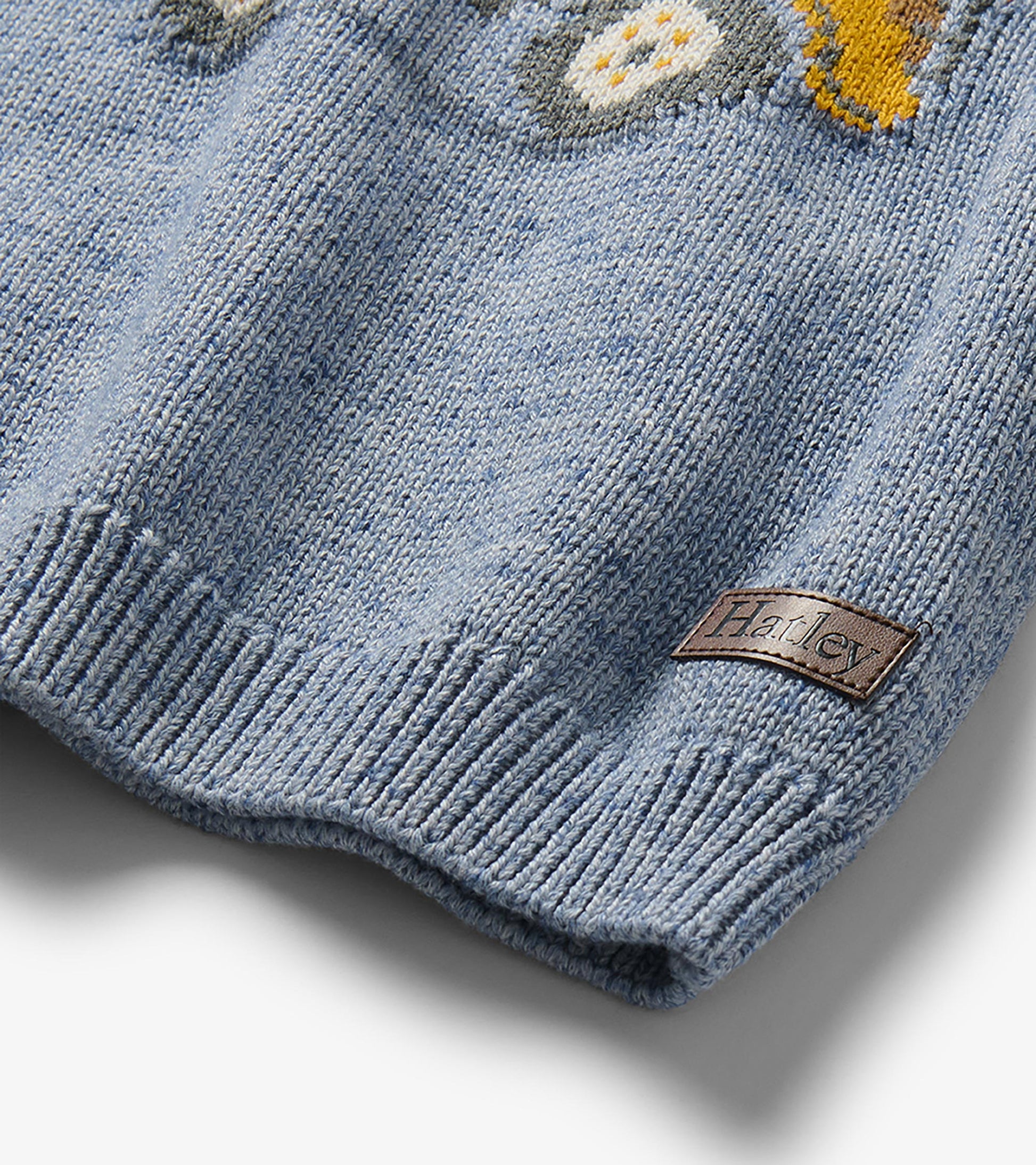 Close-up of heathered blue sweater hem with ribbed knit, partial dump truck graphic, and Hatley logo patch
