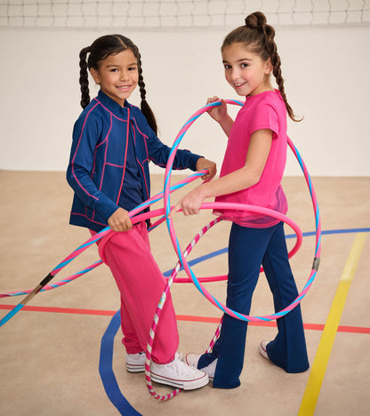 Girl wearing blue active jacket with pink stitching, standing with hula hoops in a gym