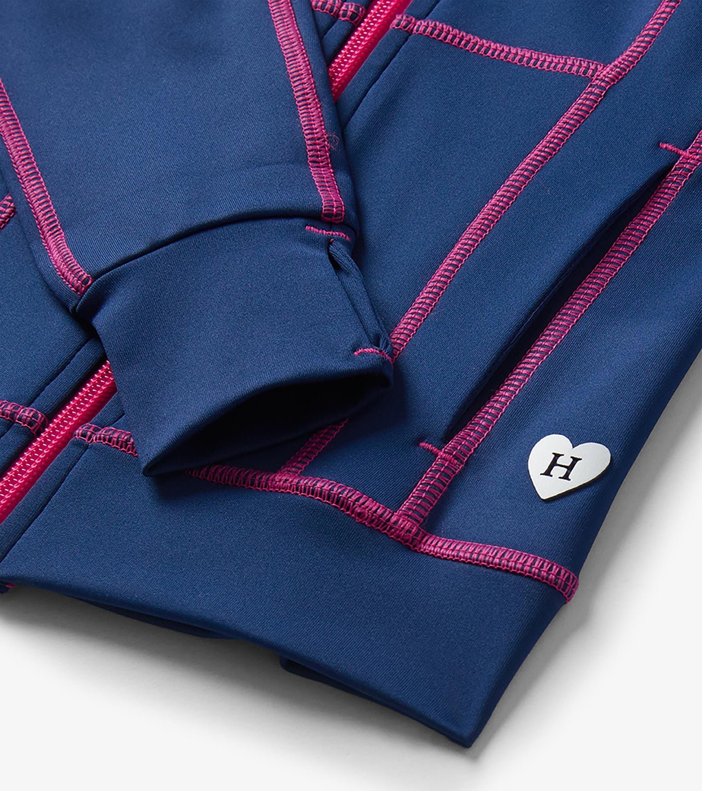 Close-up of blue active jacket cuff with thumbhole, pink stitching, zipper, and heart-shaped H logo