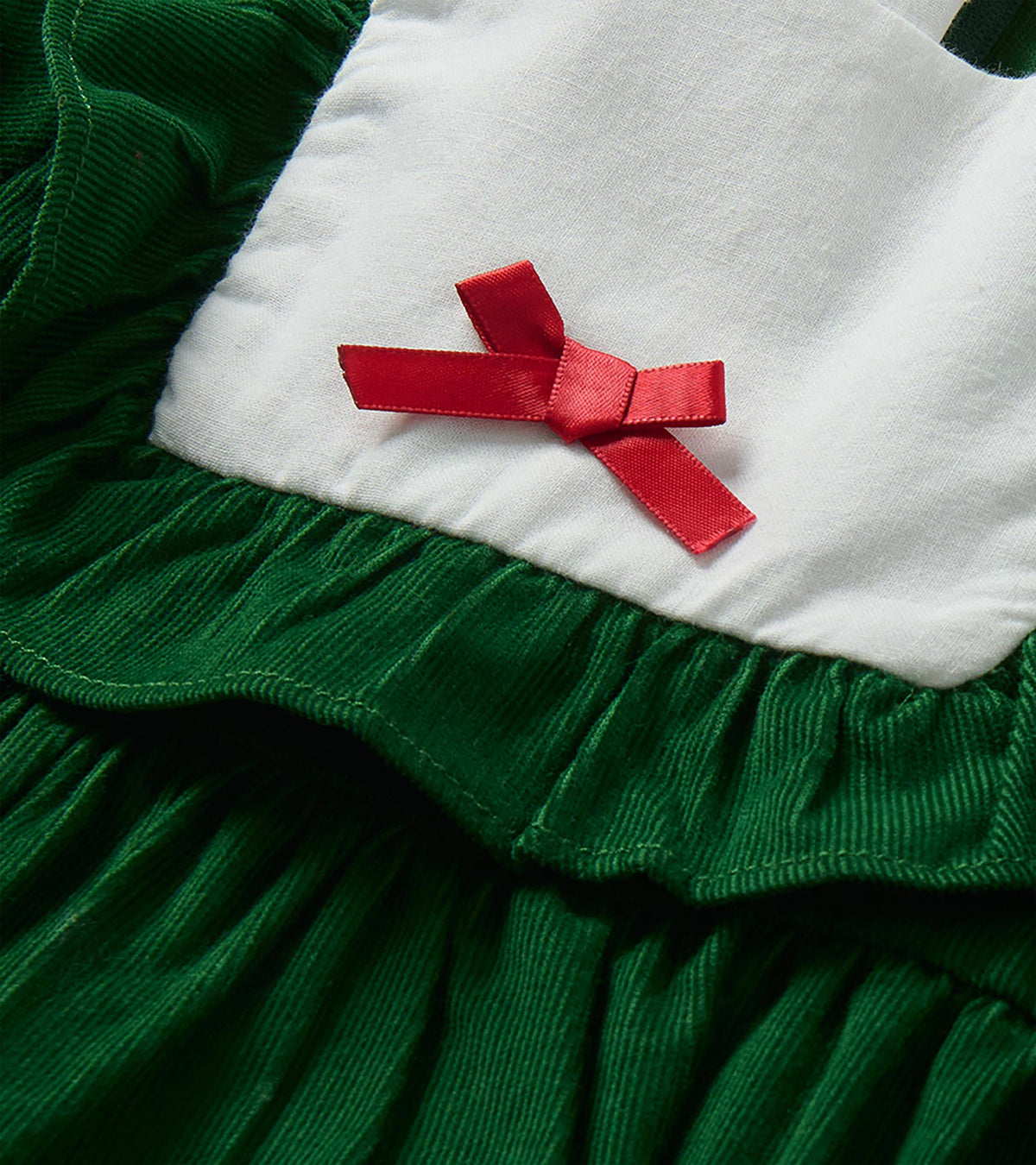 Close-up of red bow on white bib collar with green ruffle trim and textured green fabric