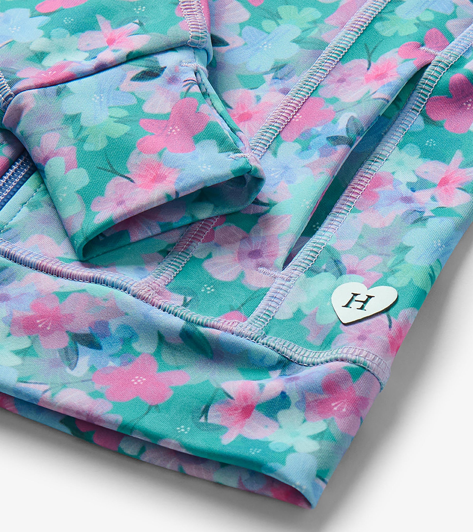 Close-up of floral active jacket showing seam pocket, lavender stitching, and heart-shaped H charm