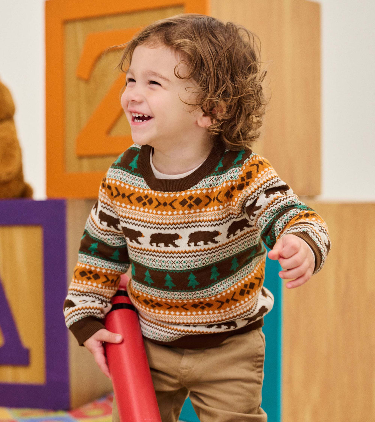 Toddler wearing brown sweater with bear and tree pattern, shown in a side angle
