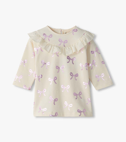 Front view of cream infant dress with pink foil bow print, ruffle yoke, and long sleeves