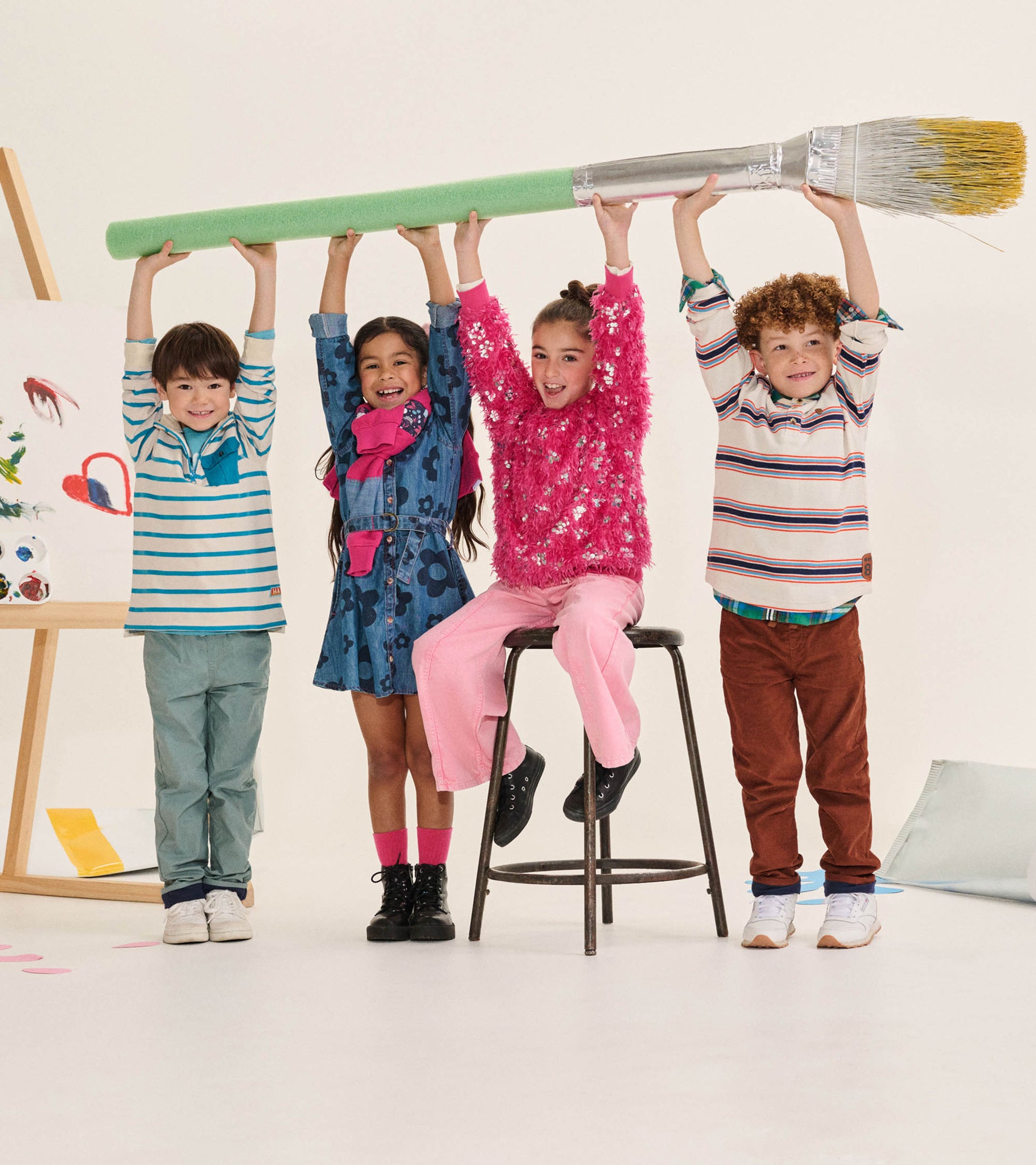 Girl wearing flamingo pink wide leg jeans and a bright pink sweater, seated beneath a giant paintbrush