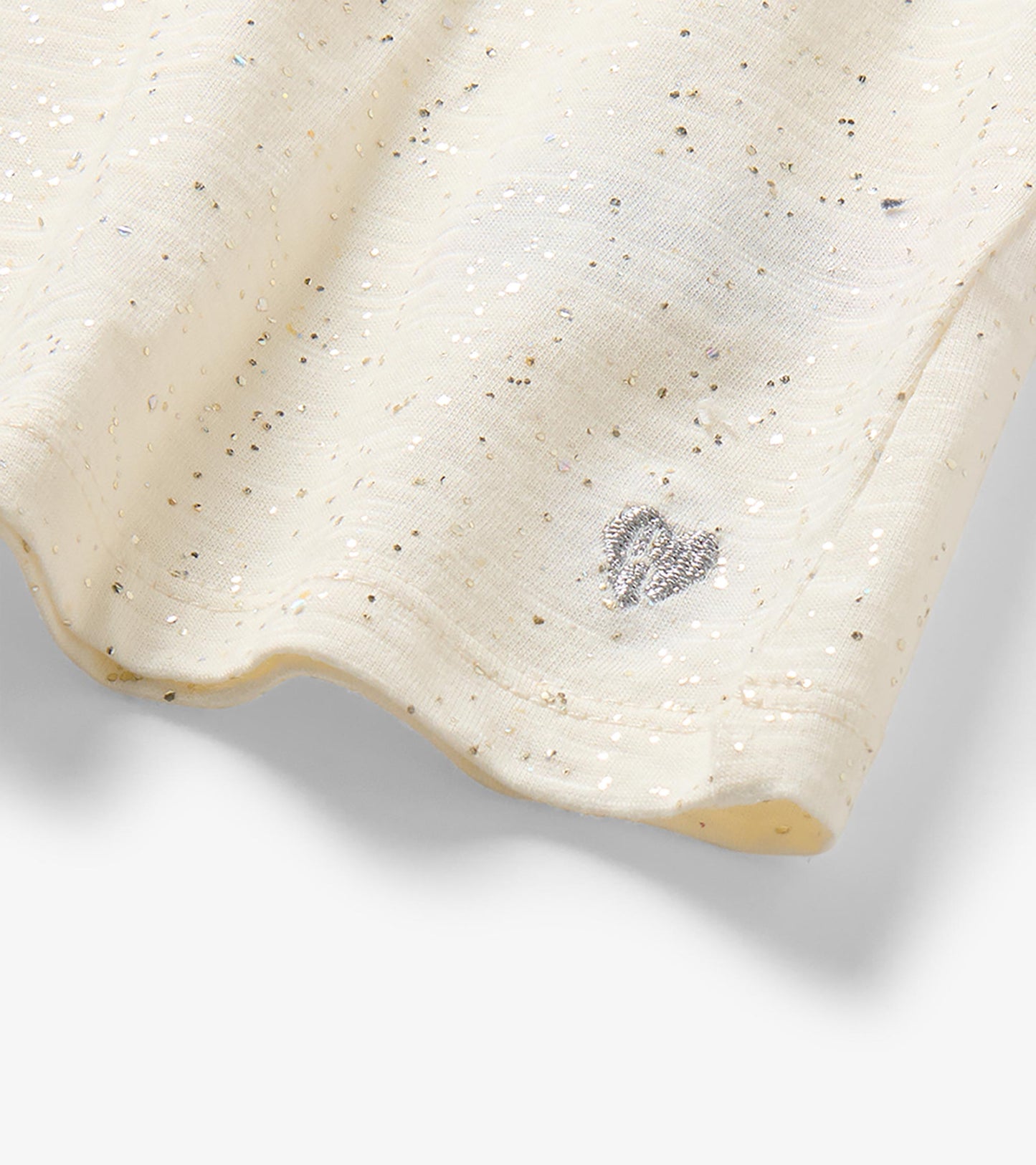 Close-up of cream glitter-speckled hem with a small silver heart detail