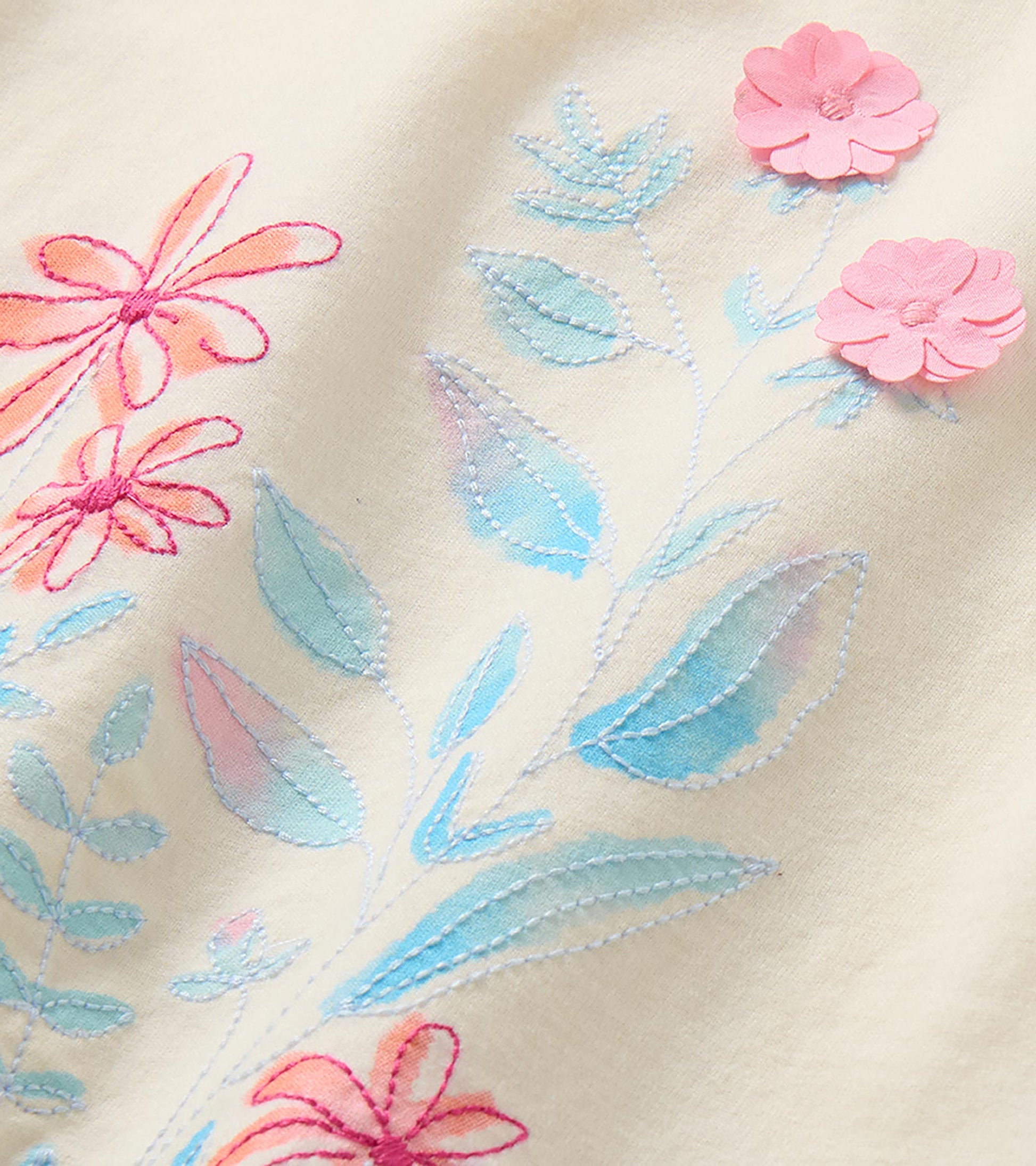Close-up of pink flower appliques and blue embroidered leaves on the cream T-shirt