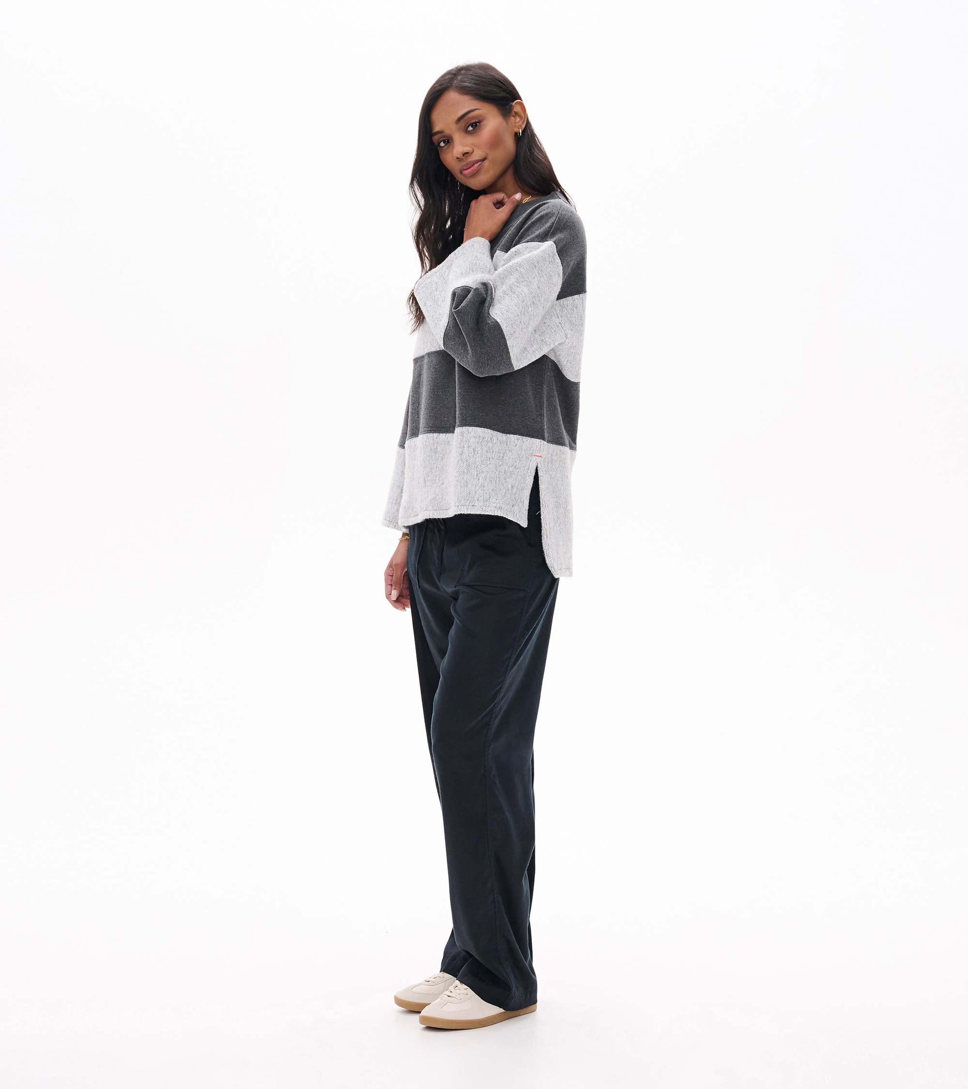 Side view of charcoal and light gray striped long sleeve top with wide sleeves and side slit hem