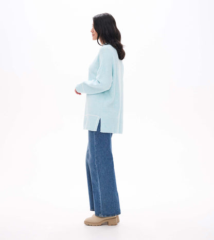 Side view of teal tunic sweater with drop shoulders, side slit and white stripe detail near the hem