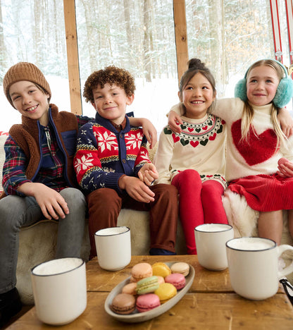 Boy wearing a navy, red, and green plaid shirt under a brown zip vest in a winter cabin scene