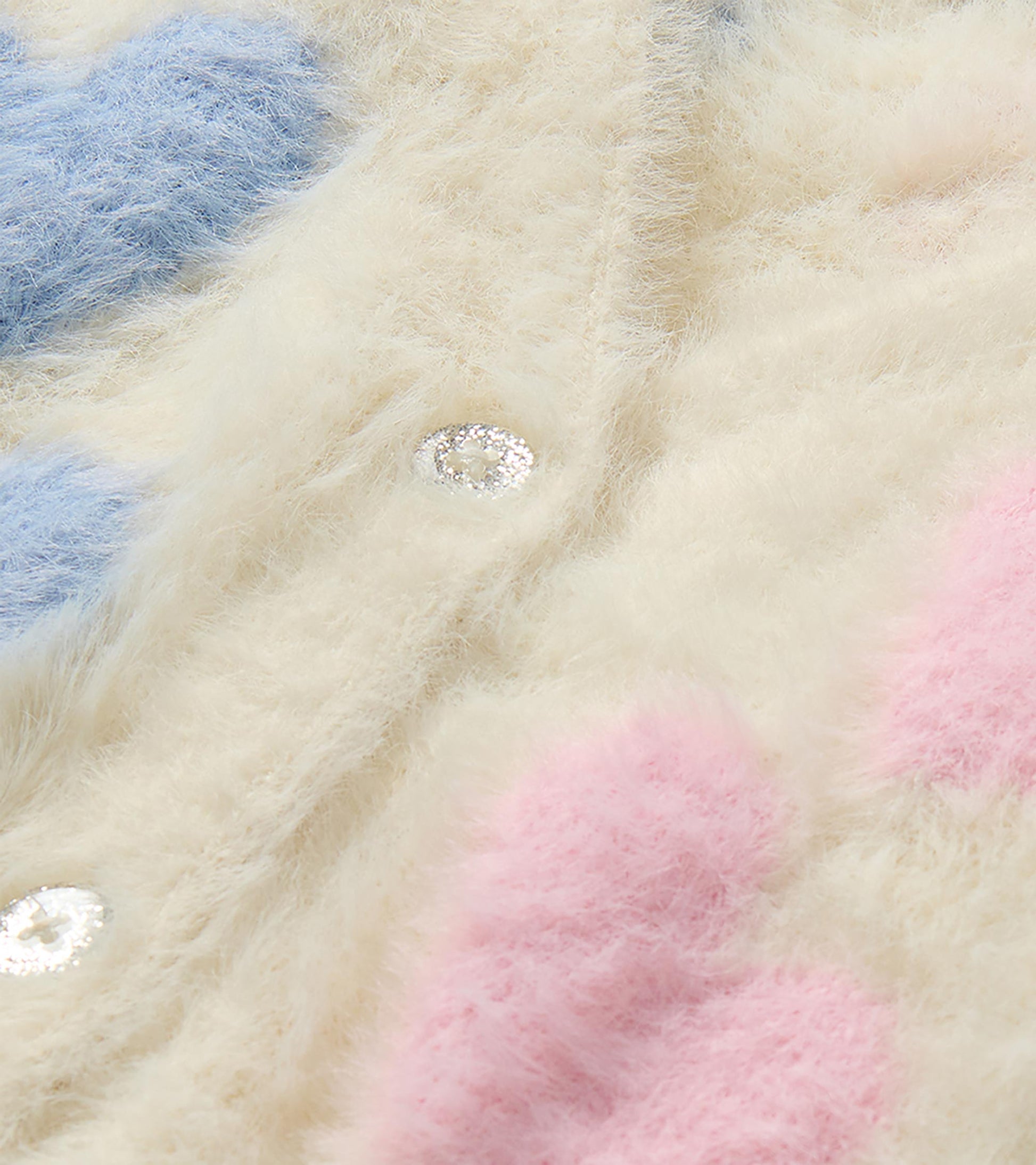 Close-up of cream fuzzy cardigan with pink and blue hearts and a glitter button detail
