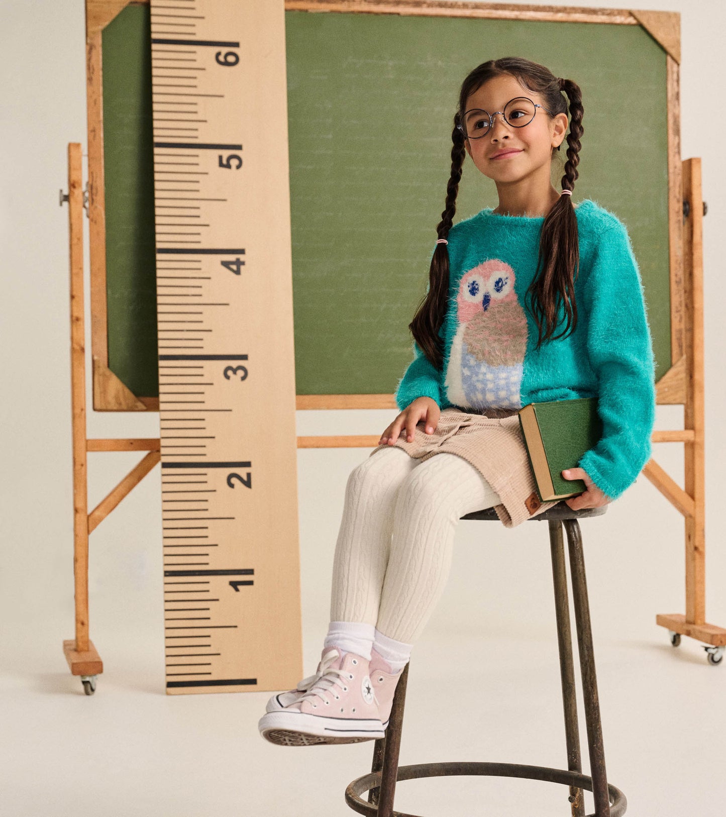 Girl seated wearing a teal fuzzy owl sweater, shown from the front