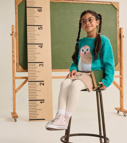 Girl seated wearing a teal fuzzy owl sweater, shown from the front