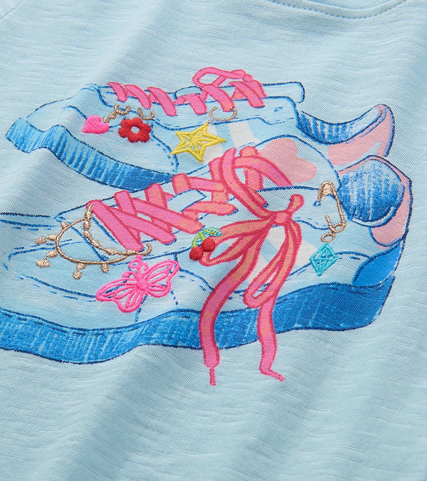 Close-up of blue sneaker graphic with pink laces and embroidered butterfly, star, flower, and charm details