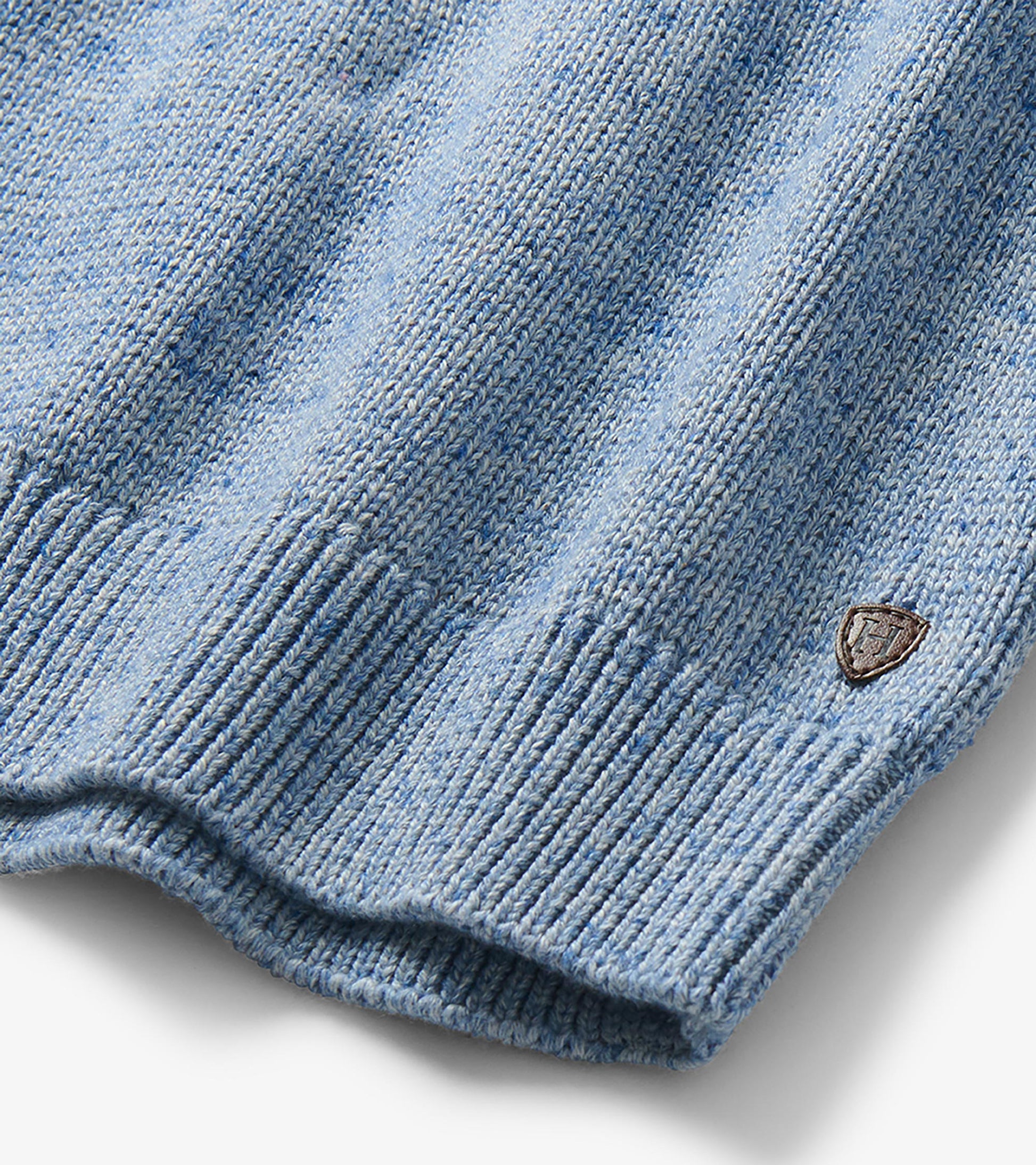 Close-up of the heathered blue knit hem with ribbed trim and small shield logo patch