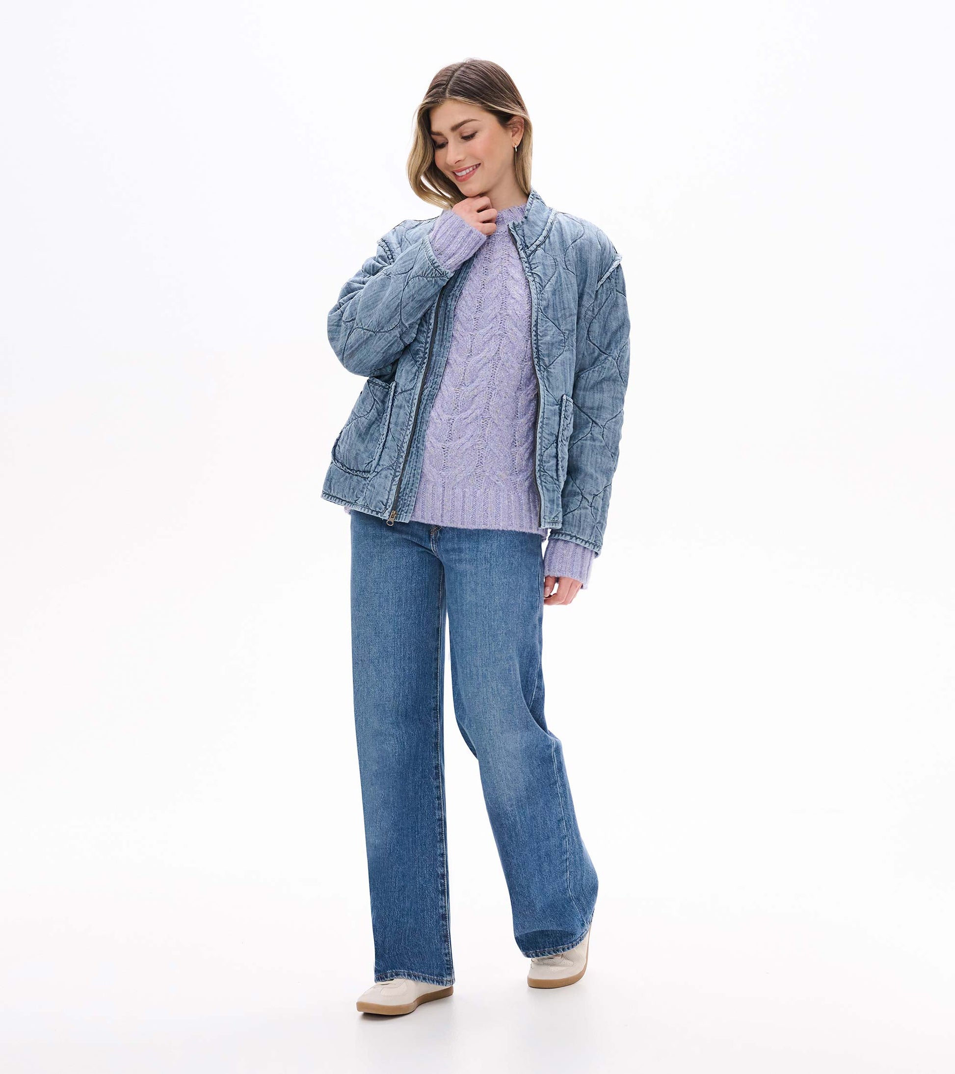 Lilac speckled cable-knit sweater worn under a faded blue quilted jacket with jeans