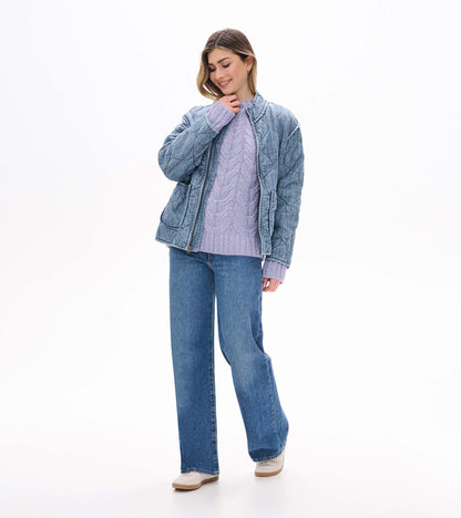 Lilac speckled cable-knit sweater worn under a faded blue quilted jacket with jeans