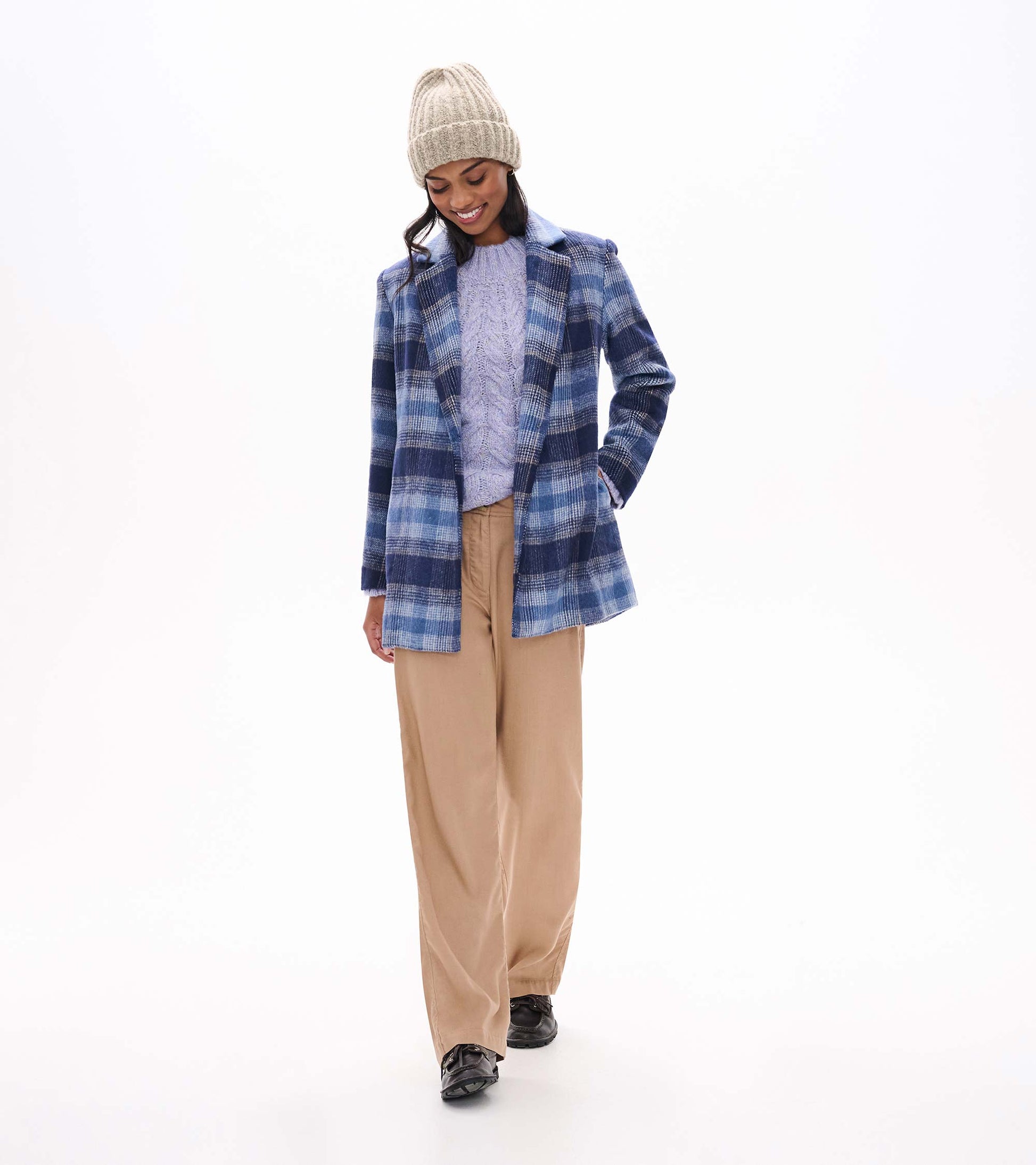Lilac speckled cable-knit sweater styled under a blue plaid coat with tan pants and a knit beanie