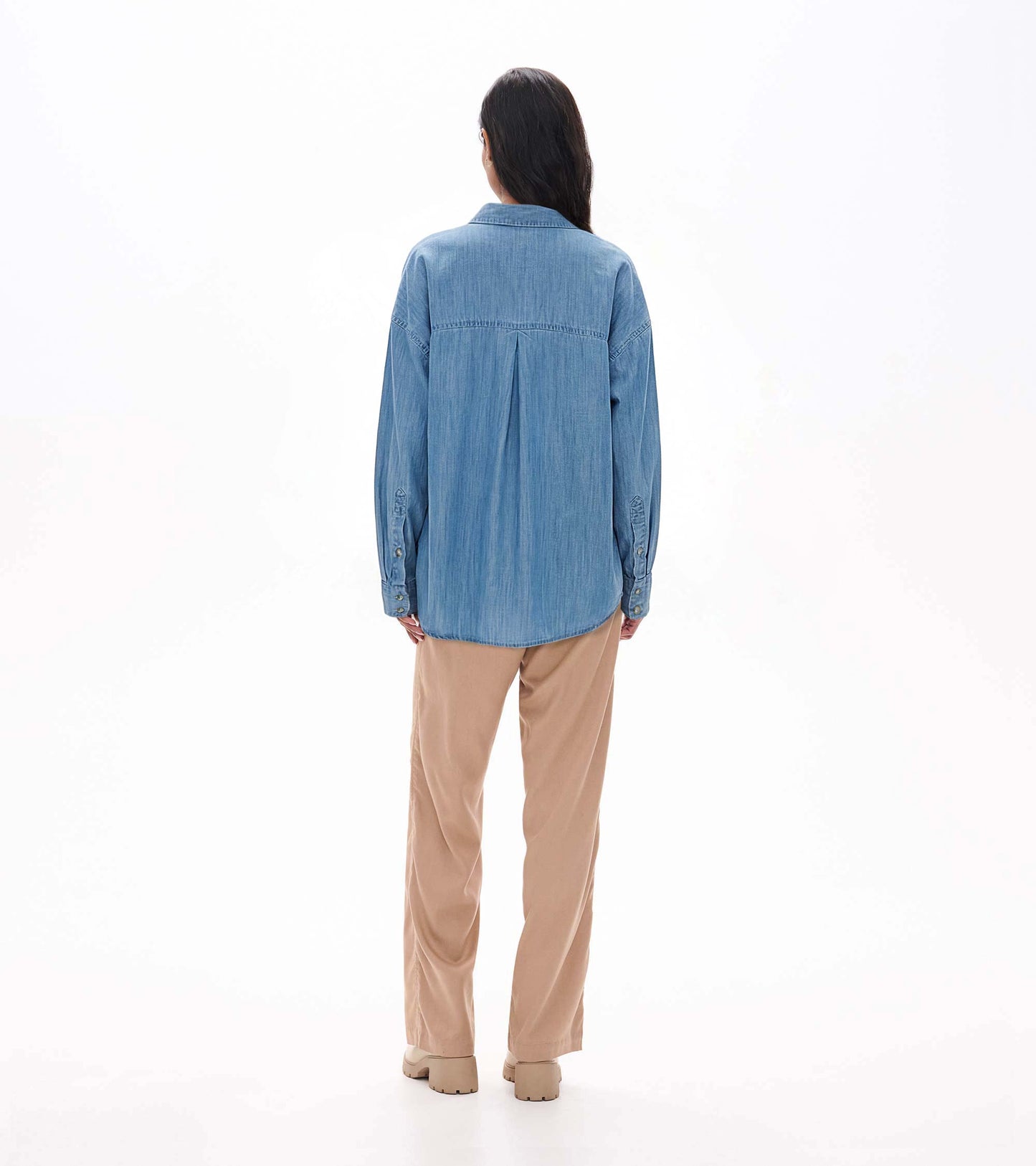Back view of relaxed light blue wash button-down shirt on model with back pleat and curved hem