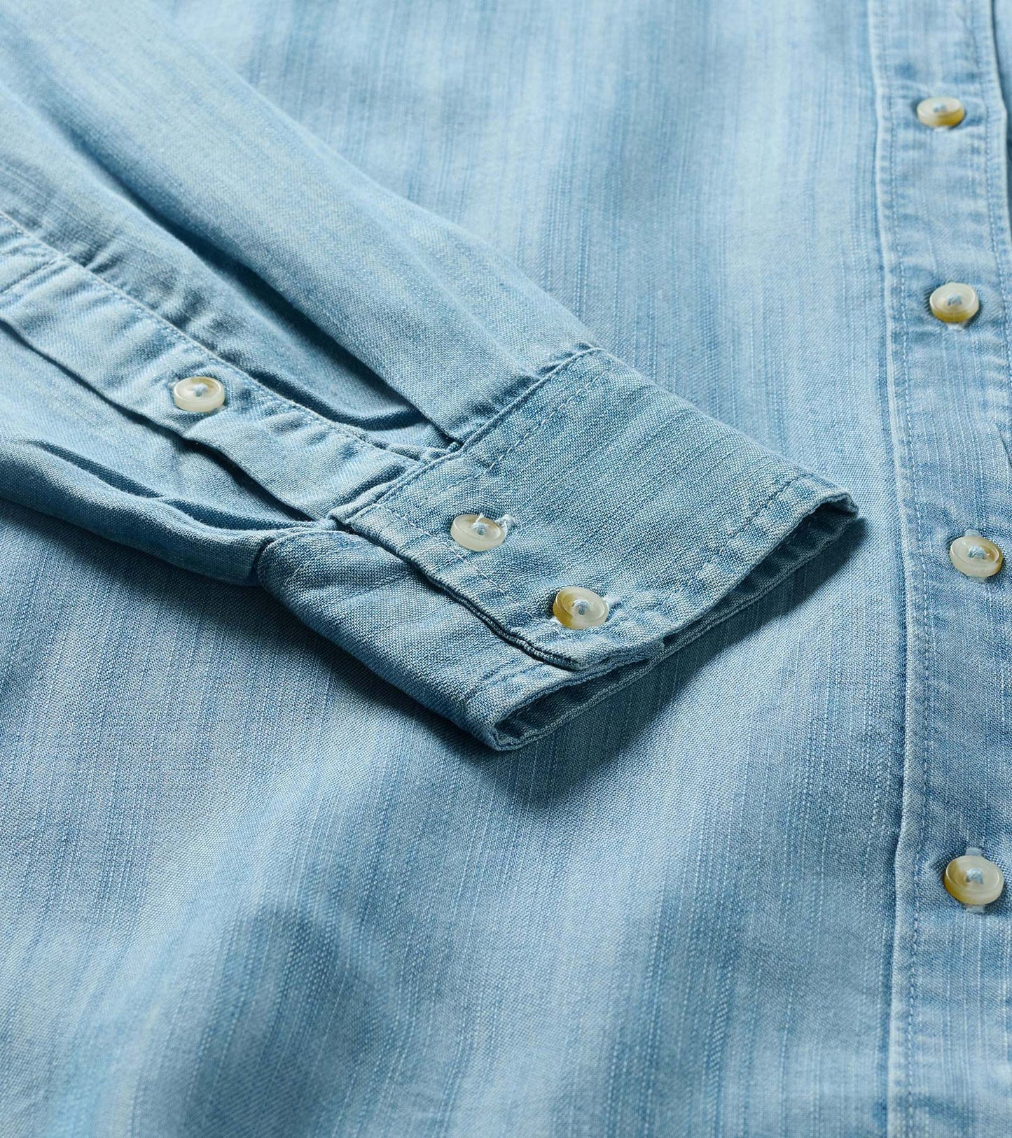 Close-up of light blue wash button-down shirt showing sleeve cuff, front placket, and cream buttons