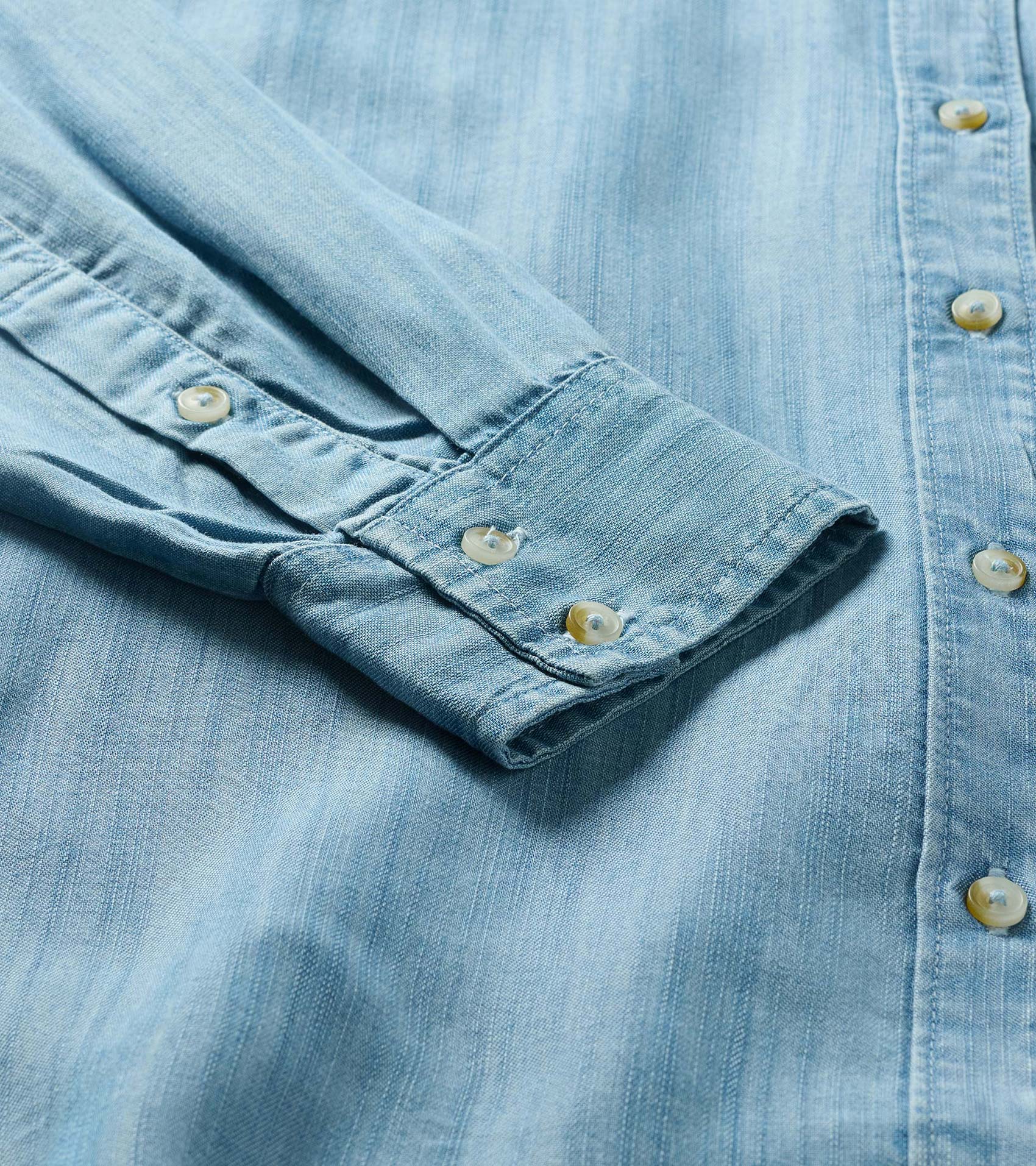 Close-up of light blue wash button-down shirt showing sleeve cuff, front placket, and cream buttons