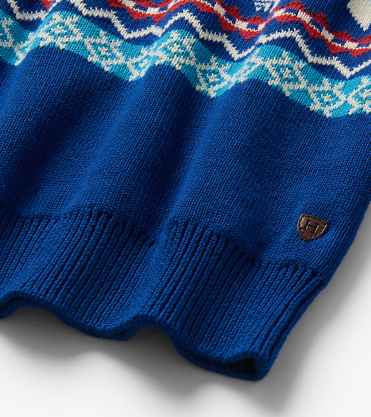 Close-up of blue sweater hem with ribbed trim, Fair Isle pattern, and small brown logo patch
