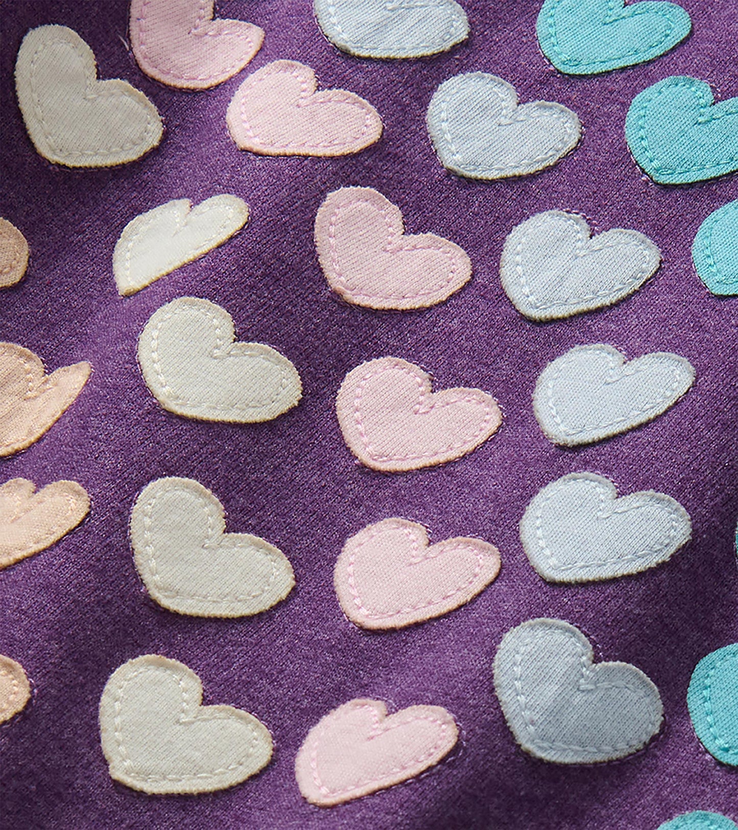 Close-up of stitched heart appliqués in pink, cream, light blue, and teal on purple fabric