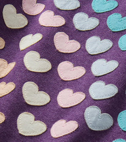 Close-up of stitched heart appliqués in pink, cream, light blue, and teal on purple fabric