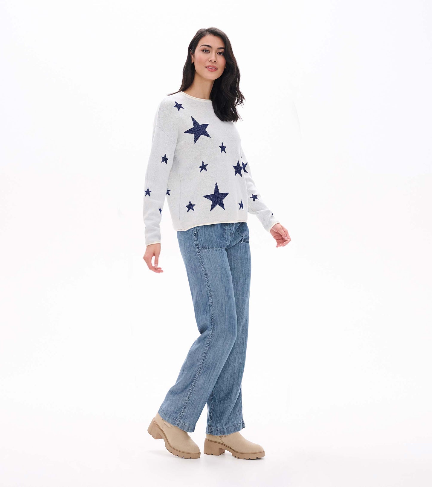 Three-quarter front view of cream sweater with navy stars, styled with wide-leg blue pants