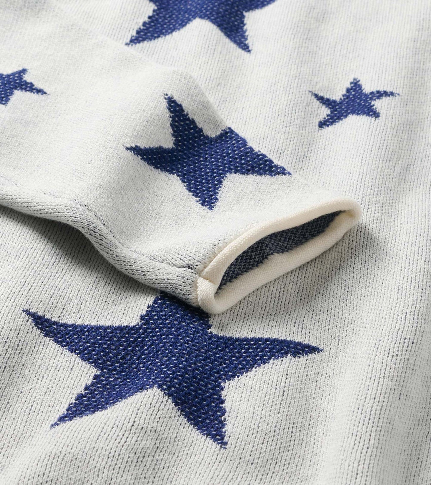 Close-up of cream sweater sleeve with rolled cuff and navy star pattern
