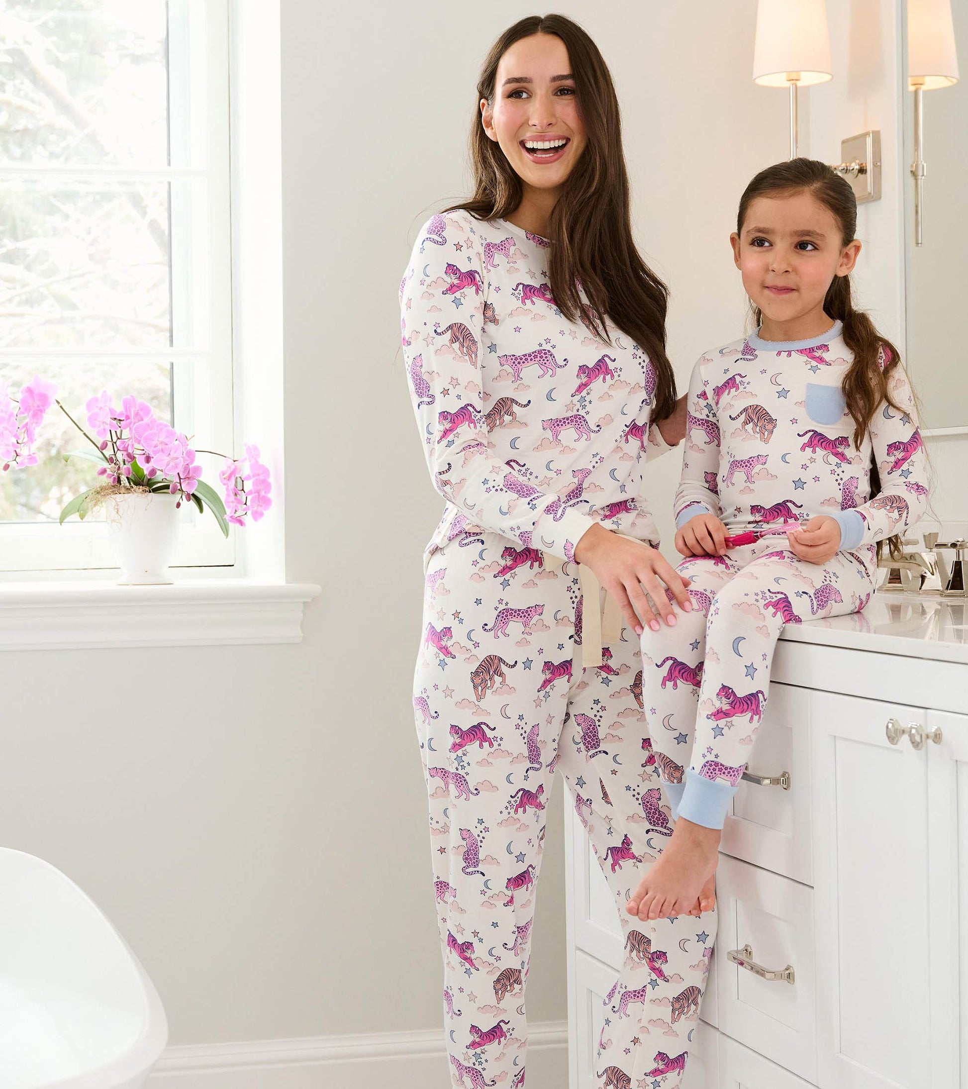 Girl and woman wearing matching tiger print pajamas with blue trim in a bright bathroom