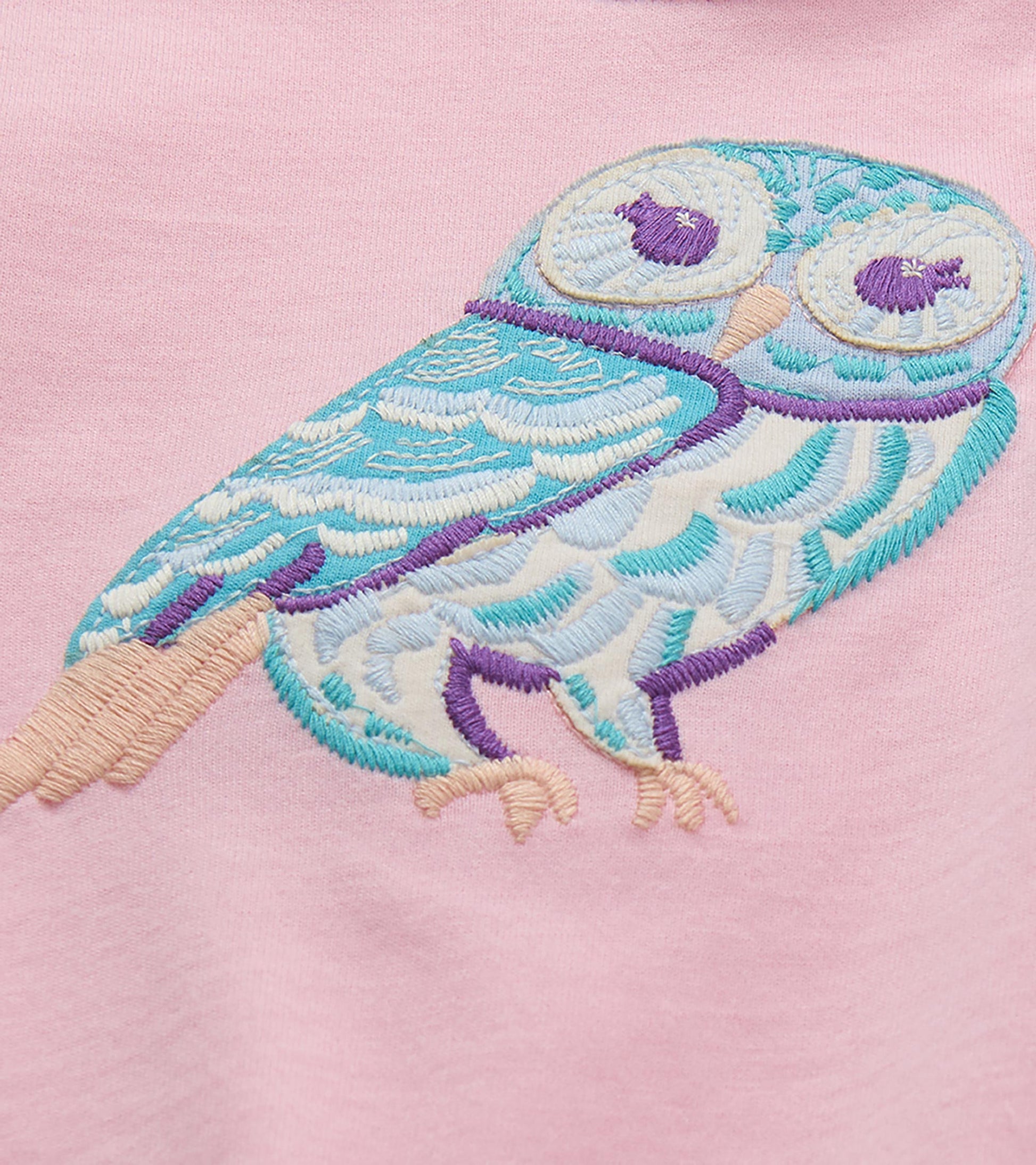 Close-up of blue, white, and purple embroidered owl on the pink T-shirt